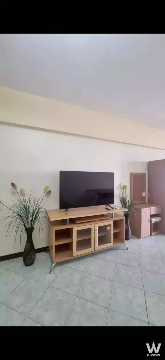 Sparsely furnished living room in 1-bed Jomtien Complex Condotel with light wood TV console and grey tiles