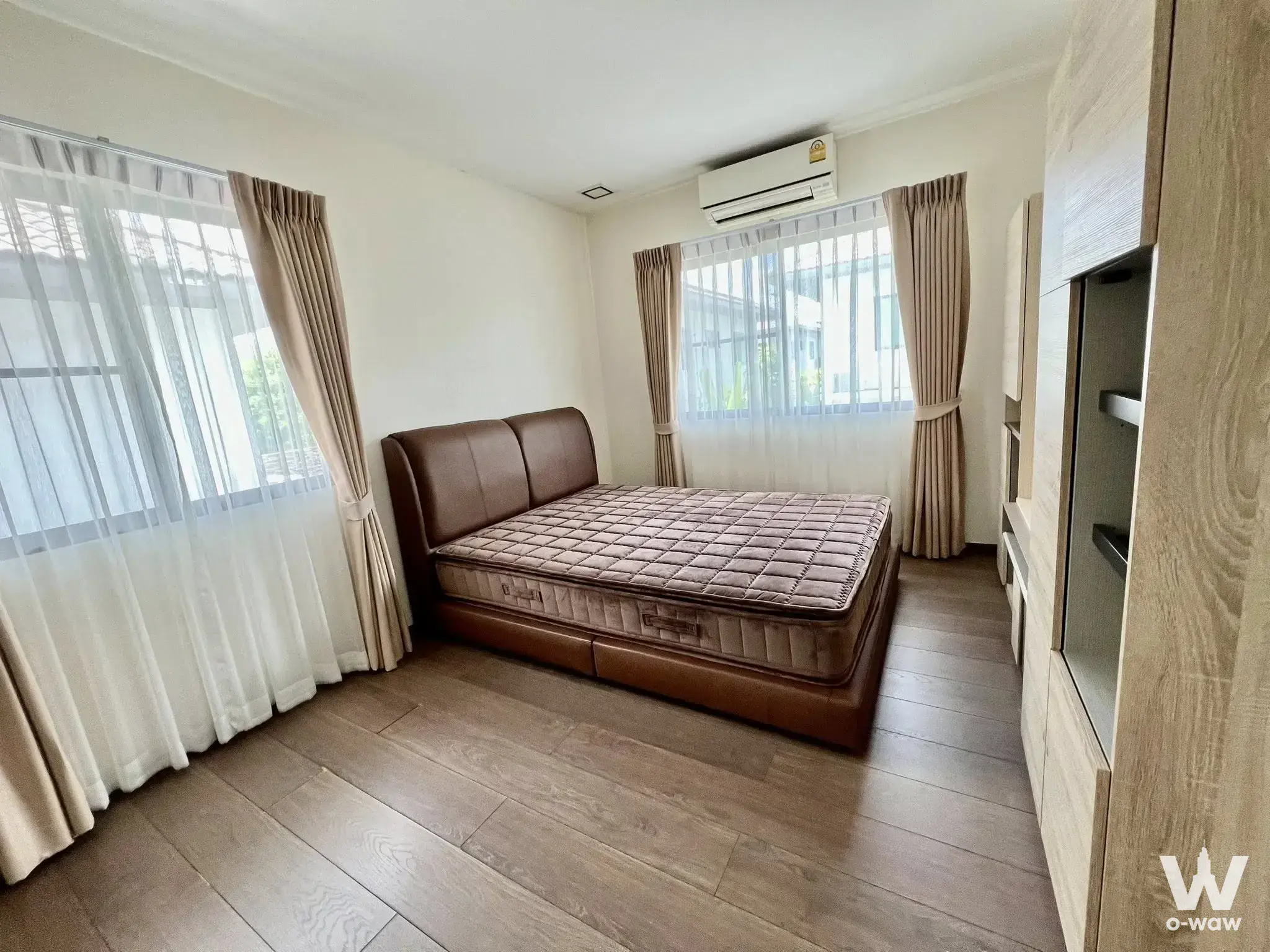 Modern bedroom with brown leather bed and light wood wardrobe overlooking city greenery