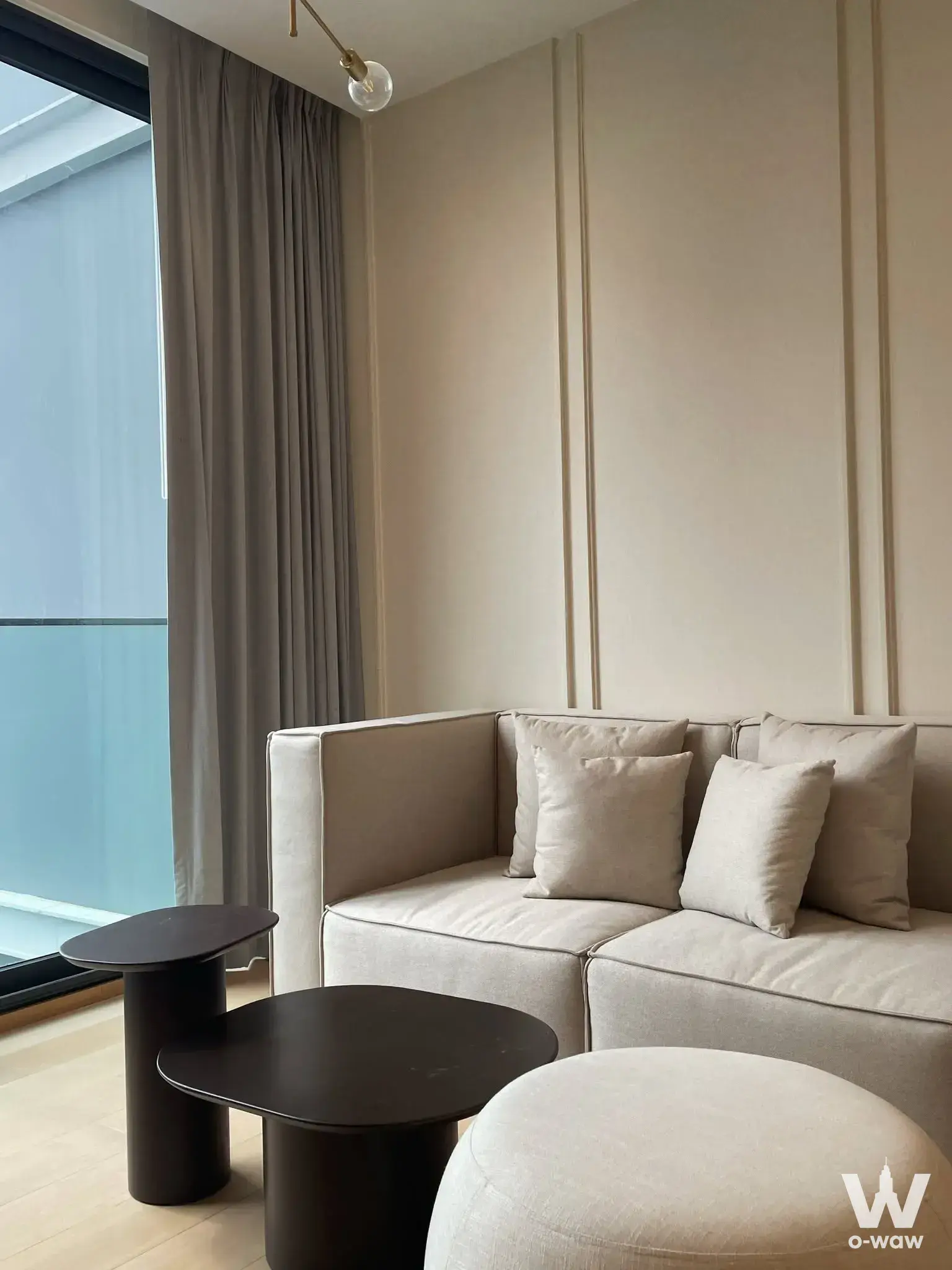 Bright living room in ANIL Sathon 12 with beige sofa, nested black tables, and fluted wall paneling