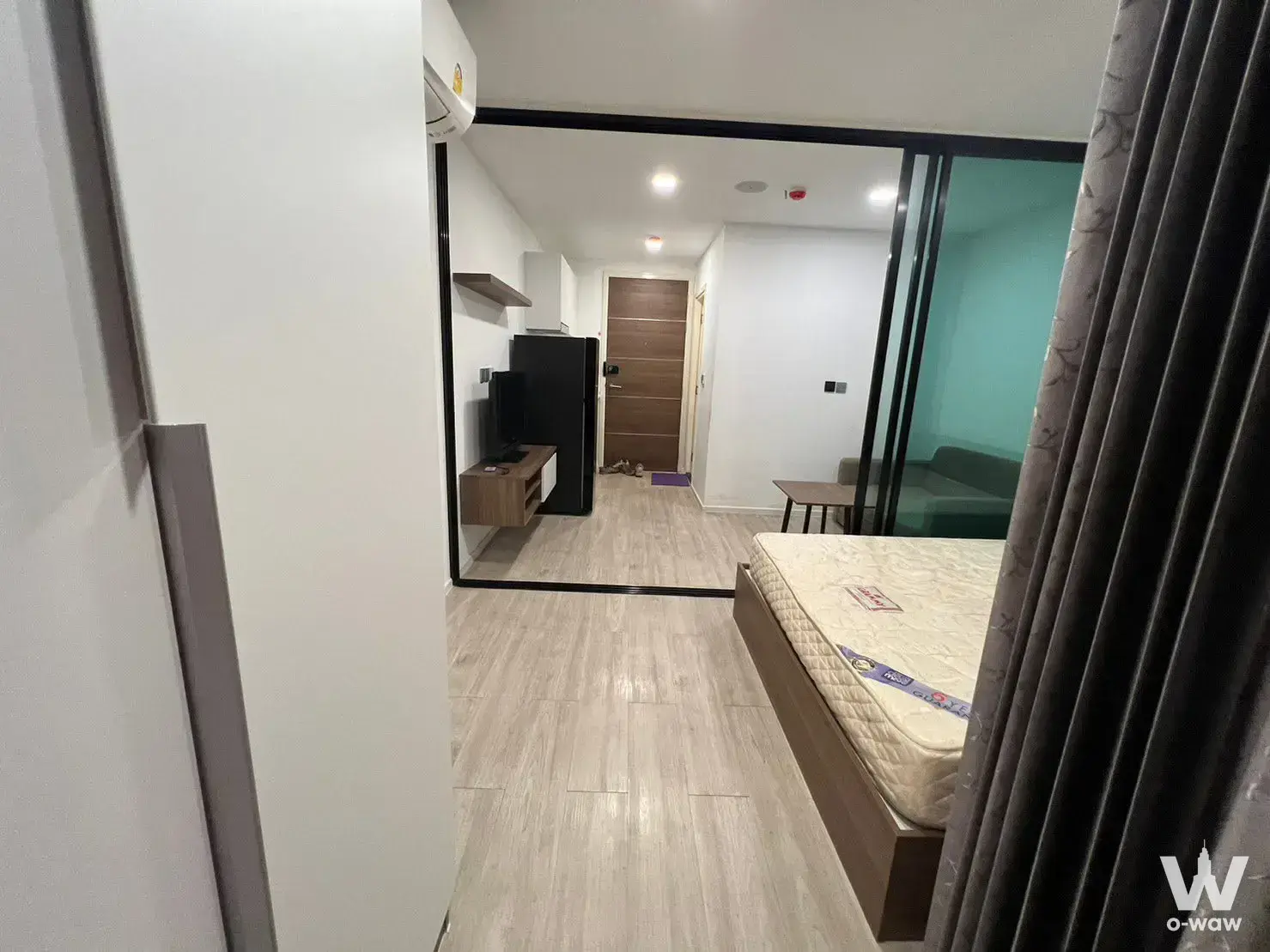 Modern 1-bed condo for sale in Atmoz Ladprao 71 with wood floors, glass partition, and green sofa