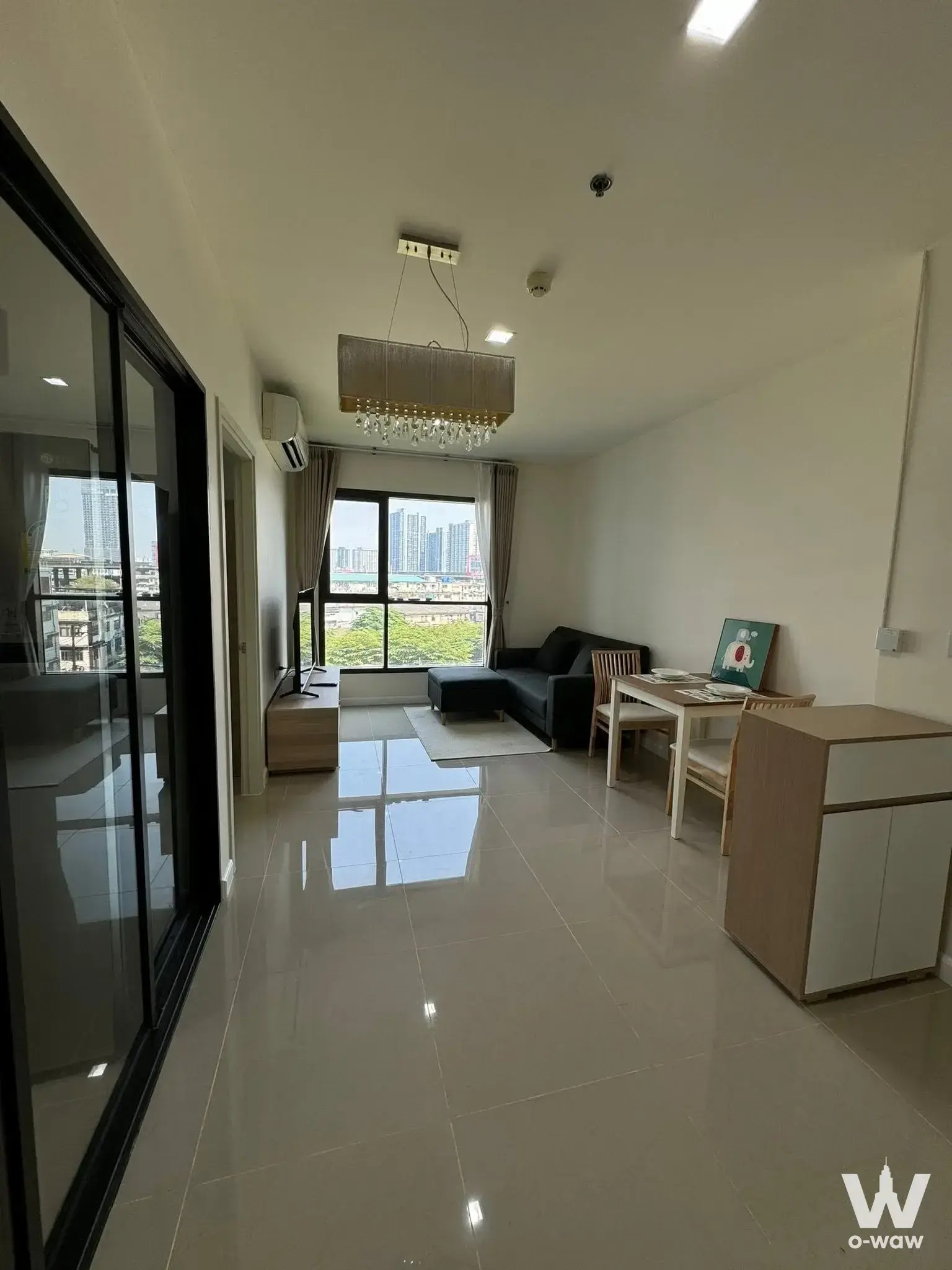 Living area in Life Sukhumvit 48 condo with grey sofa, dining set, and large windows overlooking the city skyline