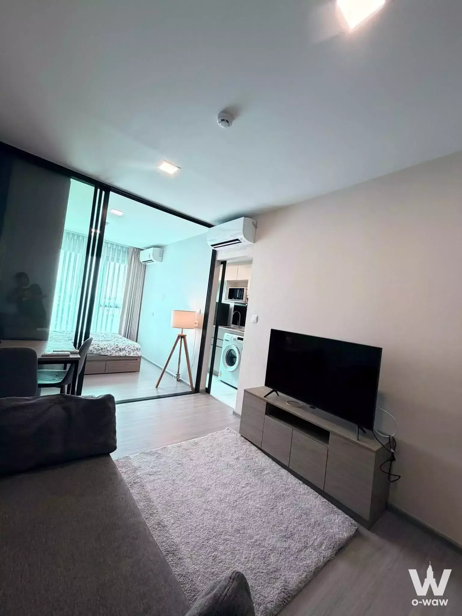 Modern 1-bed condo for rent in The Privacy S101 with charcoal sofa, oak media console, and open-plan living area