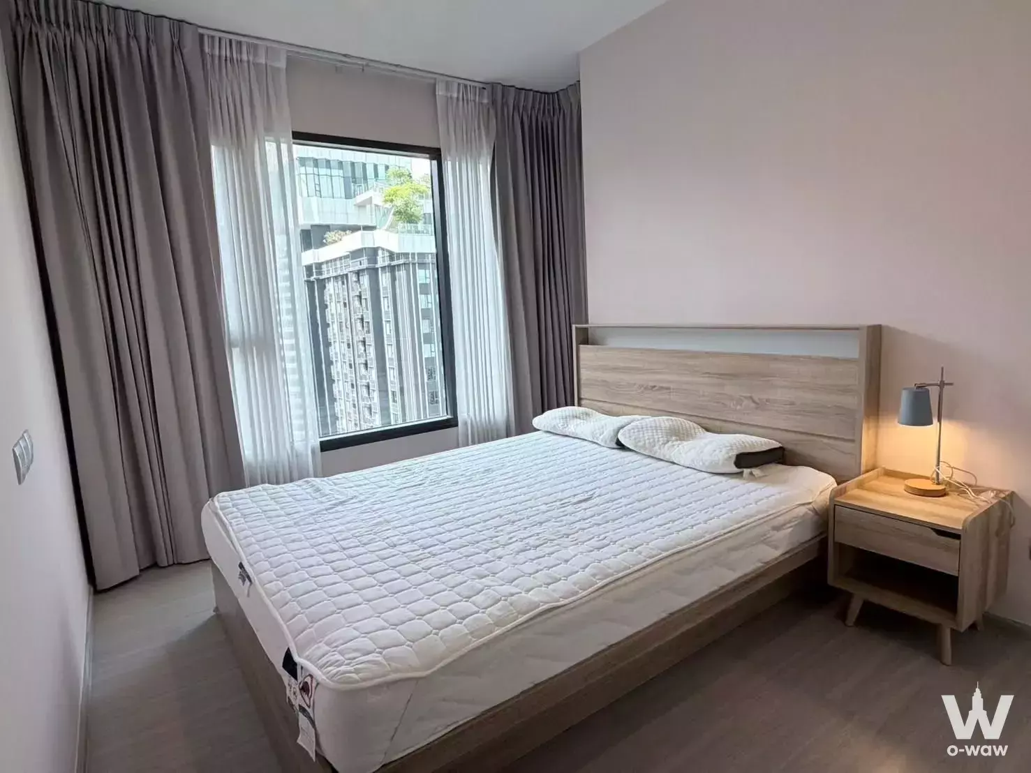 Queen bed in 1-bed condo for rent at Life Asoke Hype with oak furniture, pink walls, and city views