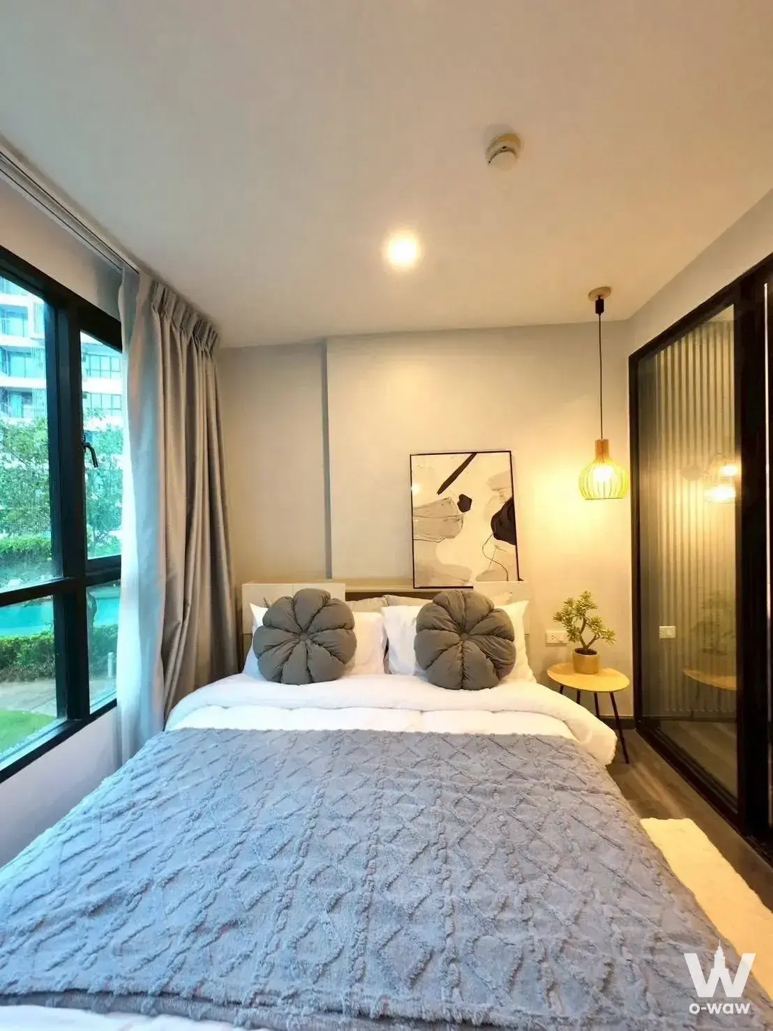 A 1-bed Centrio Phuket condo bedroom for sale has a queen bed, wood headboard and a pool-view window