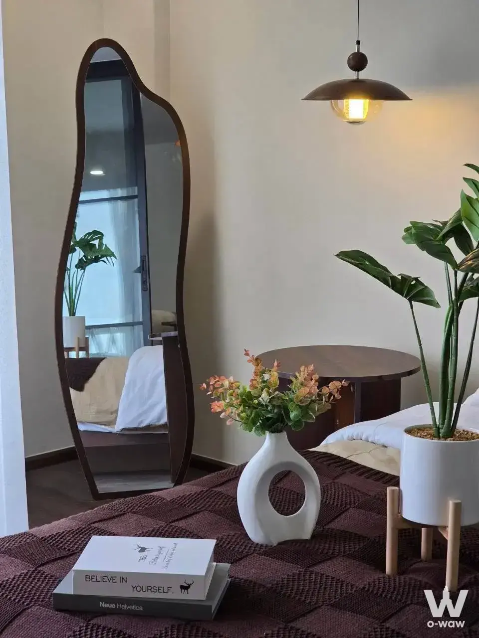 CityVilla F1 1-bed condo bedroom featuring dark brown knit bedspread, organic floor mirror, and minimalist decor