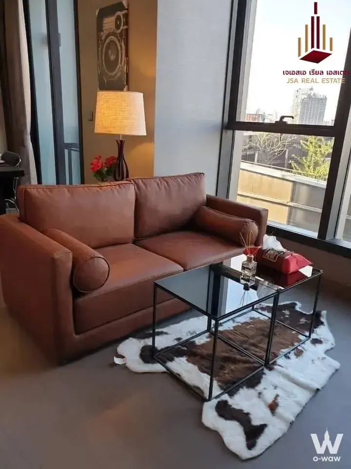 Modern living room in 1-bed condo for rent at THE ESSE ASOKE with brown leather sofa and large window view