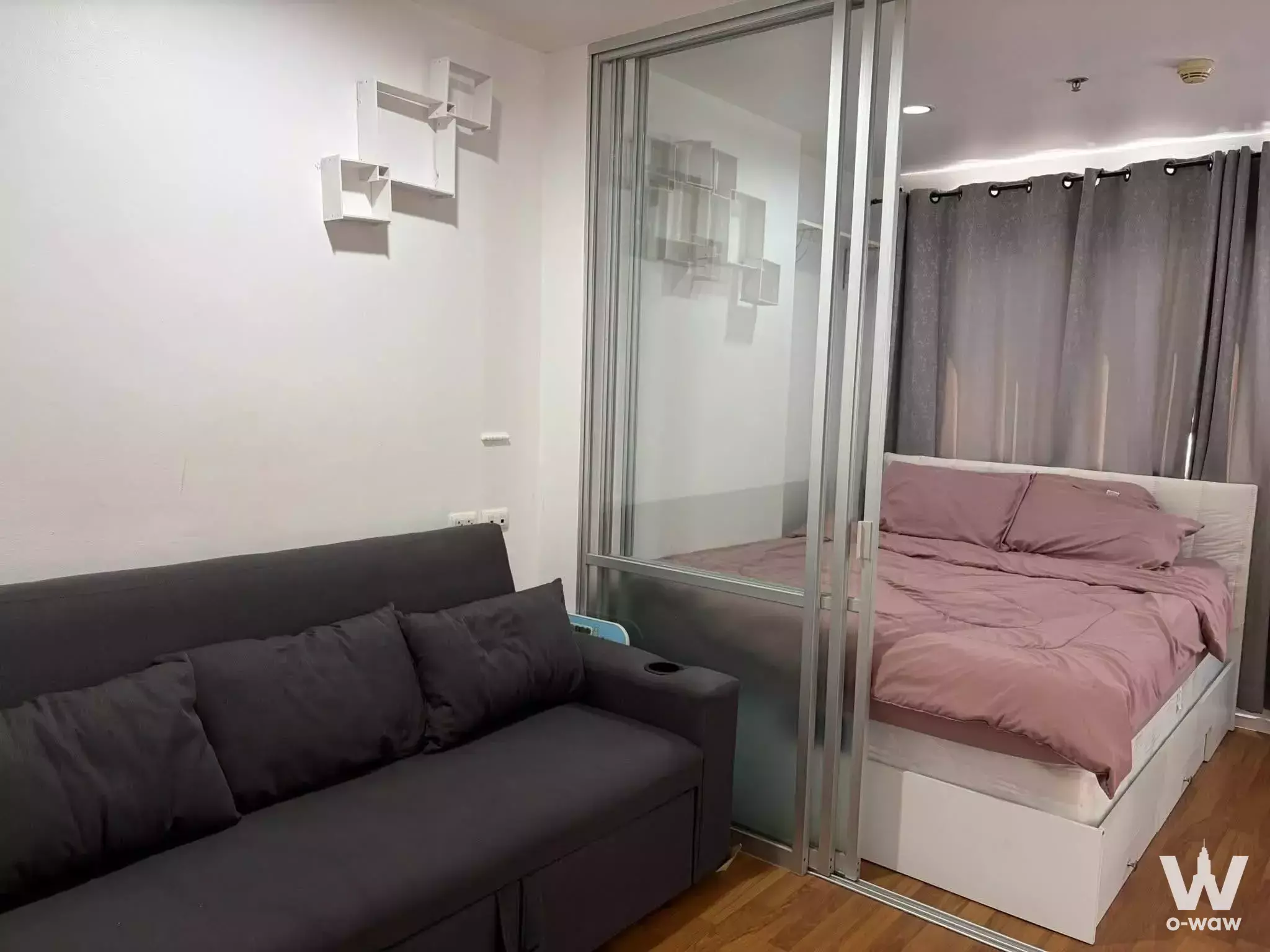 Modern 1-bed condo for rent in Lumpini Condo Town North featuring glass partition, charcoal sofa-bed, and mauve bedding