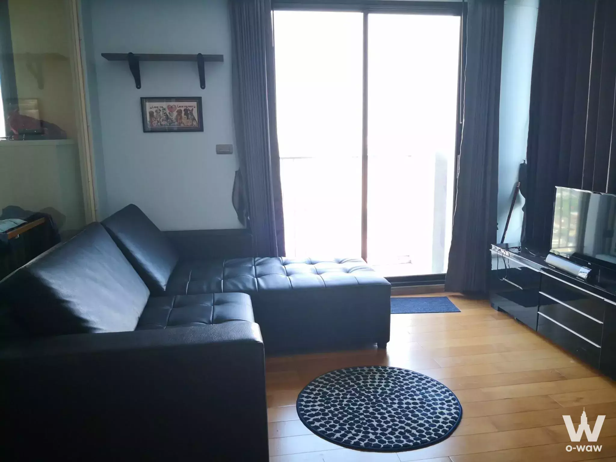 Modern living room in 1-bed Fuse Sathon-Taksin condo with black leather sofa and blue walls