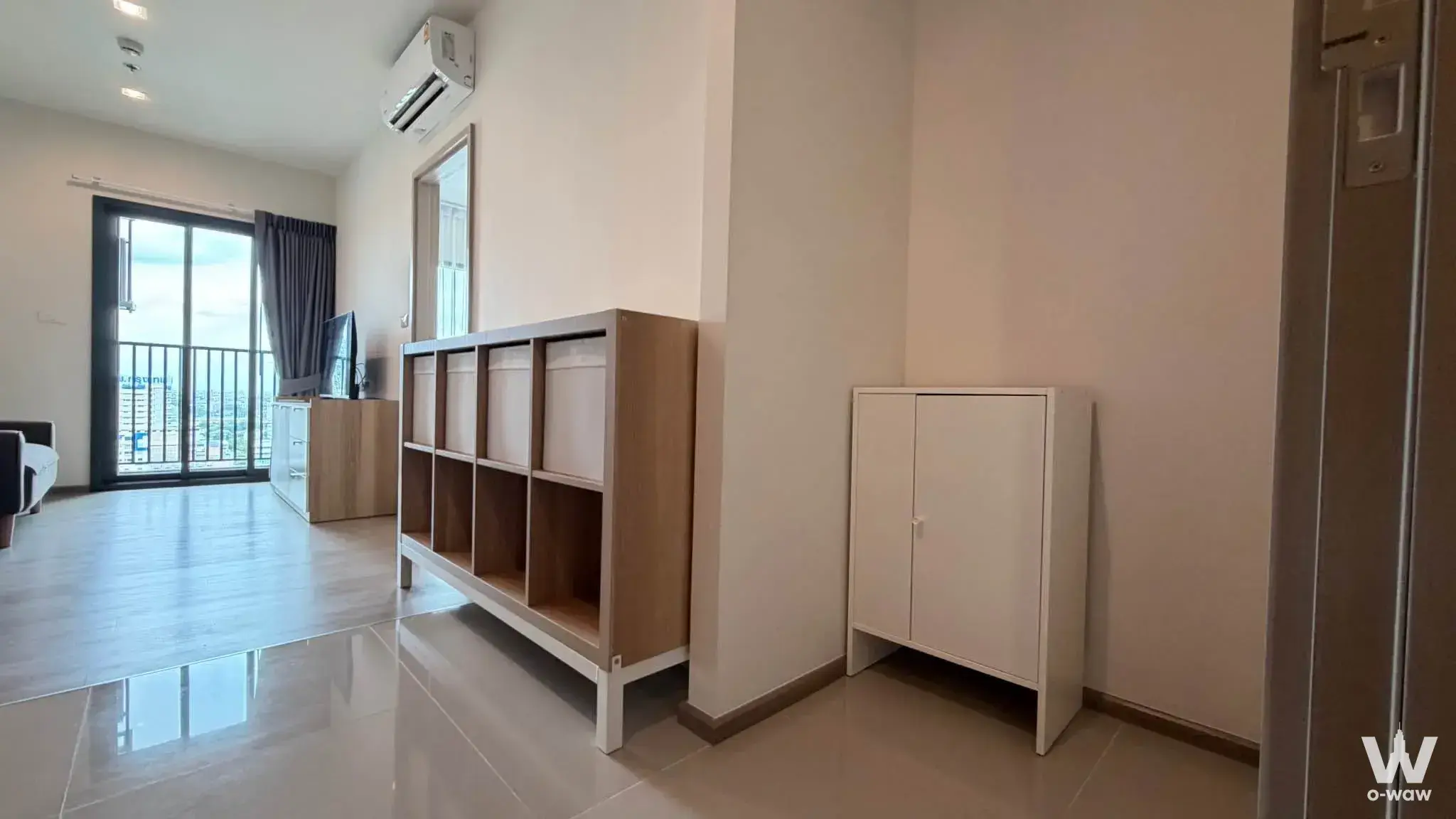 Unfurnished living room at THE BASE Phetchaburi-Thonglor with glossy tiles, wooden shelving, and balcony city views