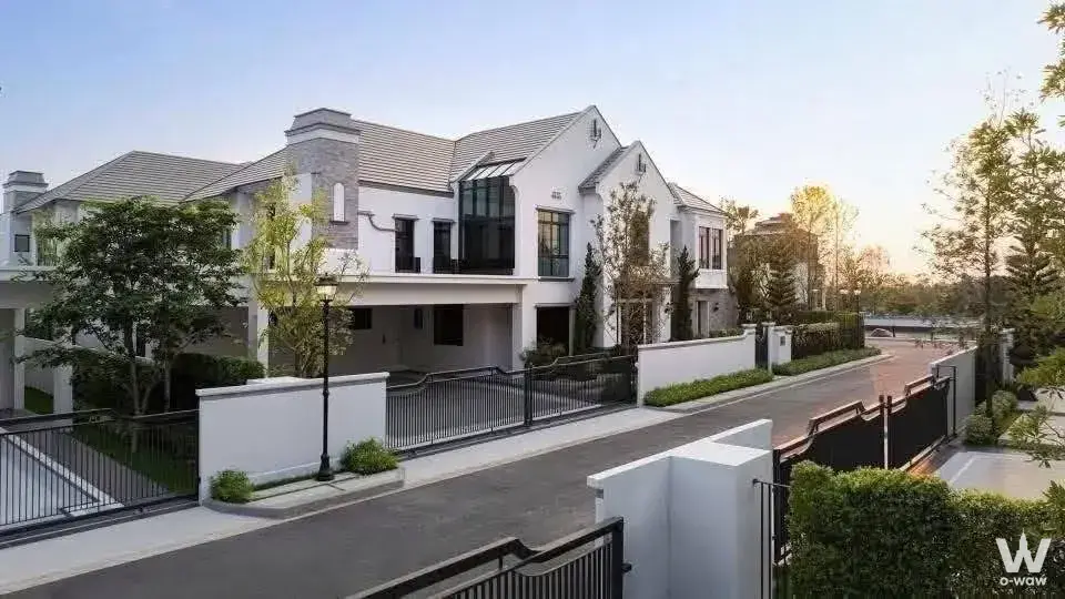 Two-story white stucco townhouse exterior with grey tiled roof and black metal gate for sale in Nantawan Bangna