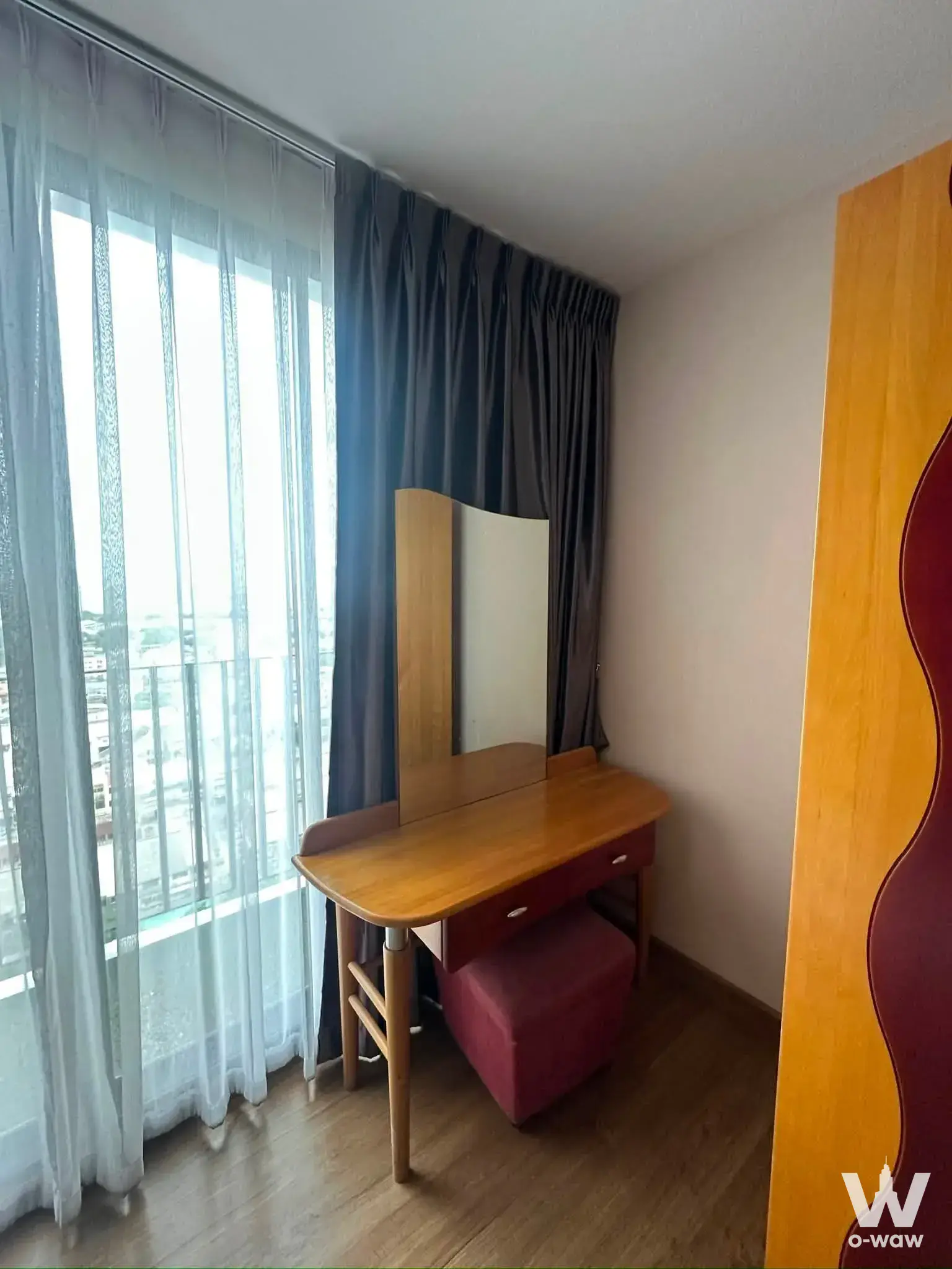 Wooden vanity with mirror and burgundy stool near glass balcony doors in 1-bed rental at The Tree Interchange Bangkok