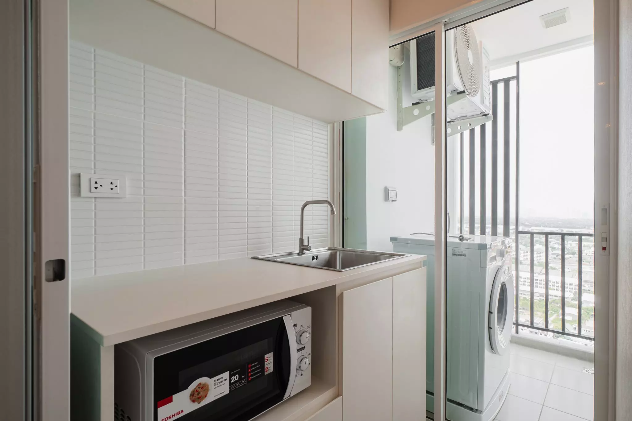 Modern kitchenette with stacked washer-dryer on utility balcony in 1-bed condo for rent at Regent Home Bangna
