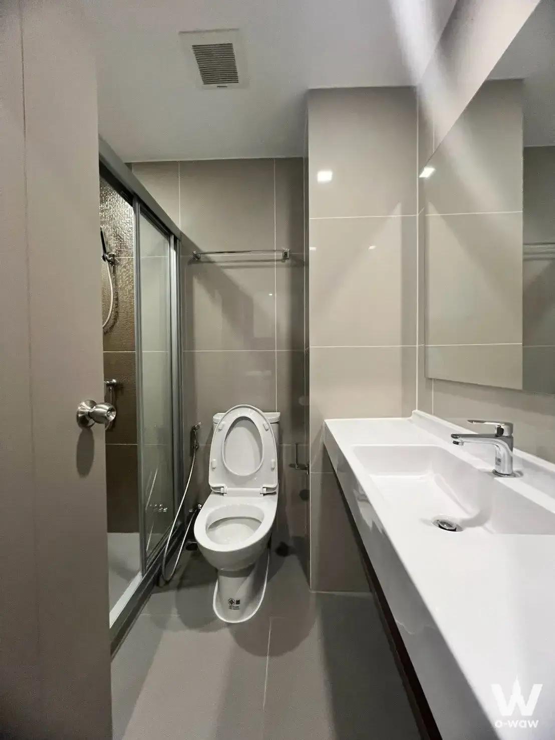 Modern bathroom in IDEO Rama 9 condo featuring glossy beige tiles, glass shower enclosure, and floating vanity