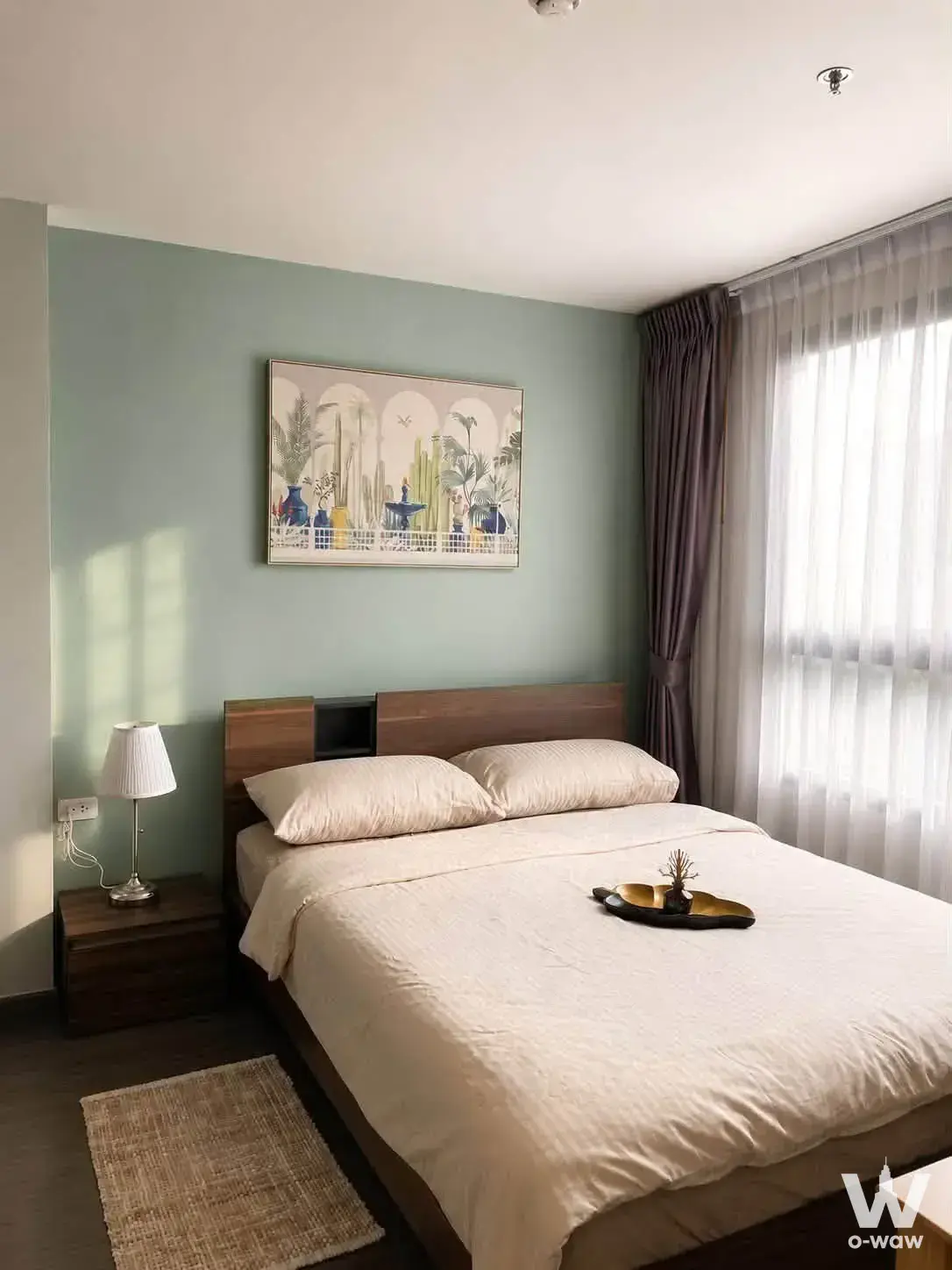 Sage green bedroom in a 1-bed Ideo Sukhumvit 93 condo with dark wood platform bed and botanical art
