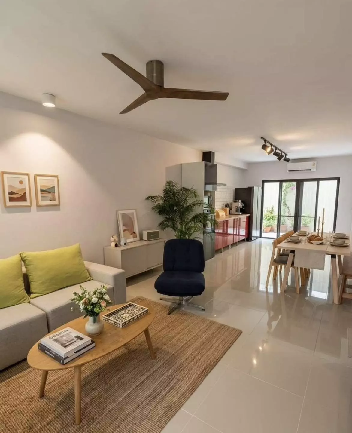 Bright living and dining area in Areeya Mandarina townhouse with white tiles, grey sofa, and red kitchen cabinets