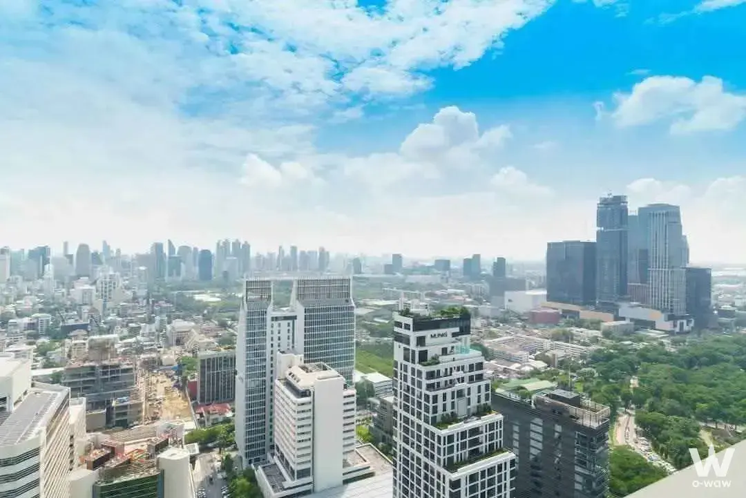 High-rise cityscape view featuring glass skyscrapers and a lush green park under a bright blue sky
