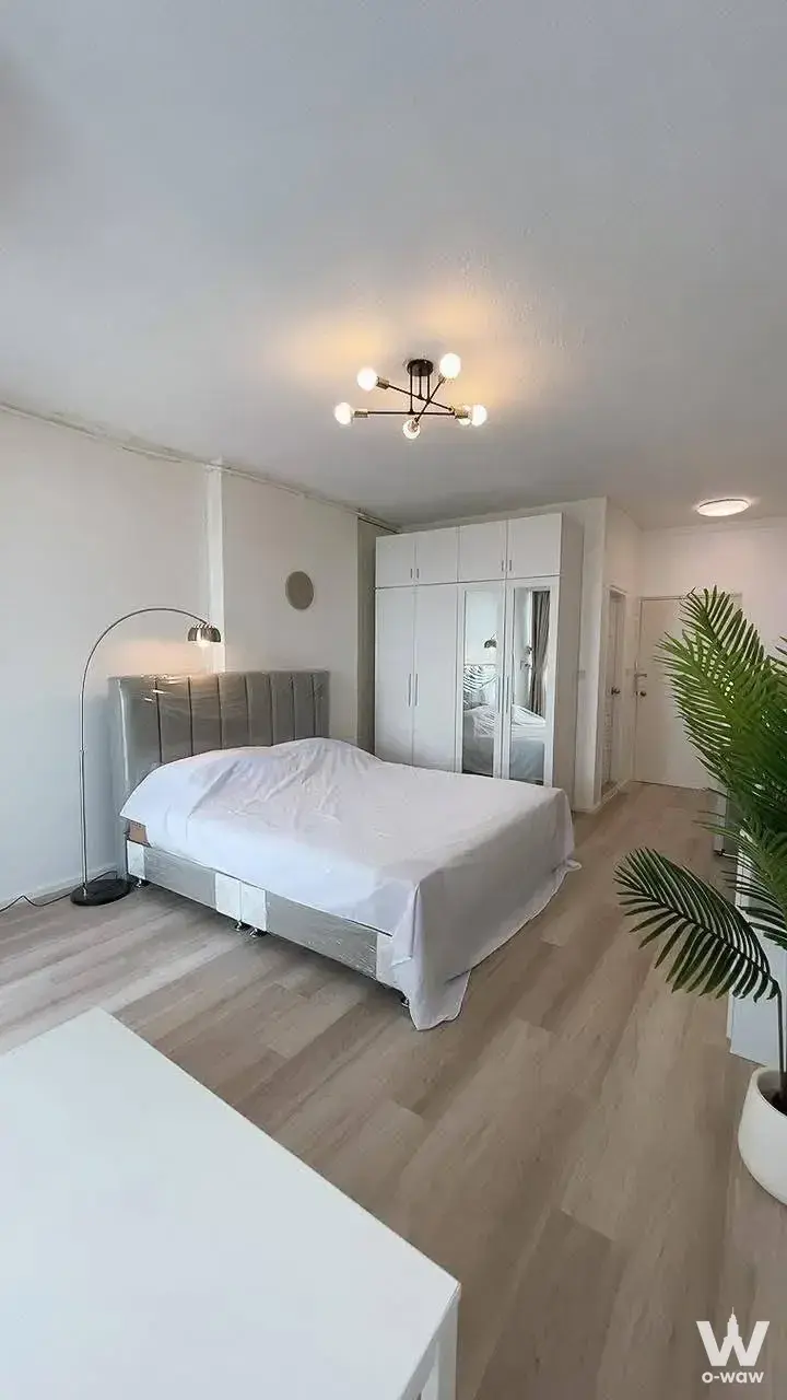 Modern bedroom with grey upholstered bed, mirrored wardrobe, and black sputnik chandelier over wood-look flooring
