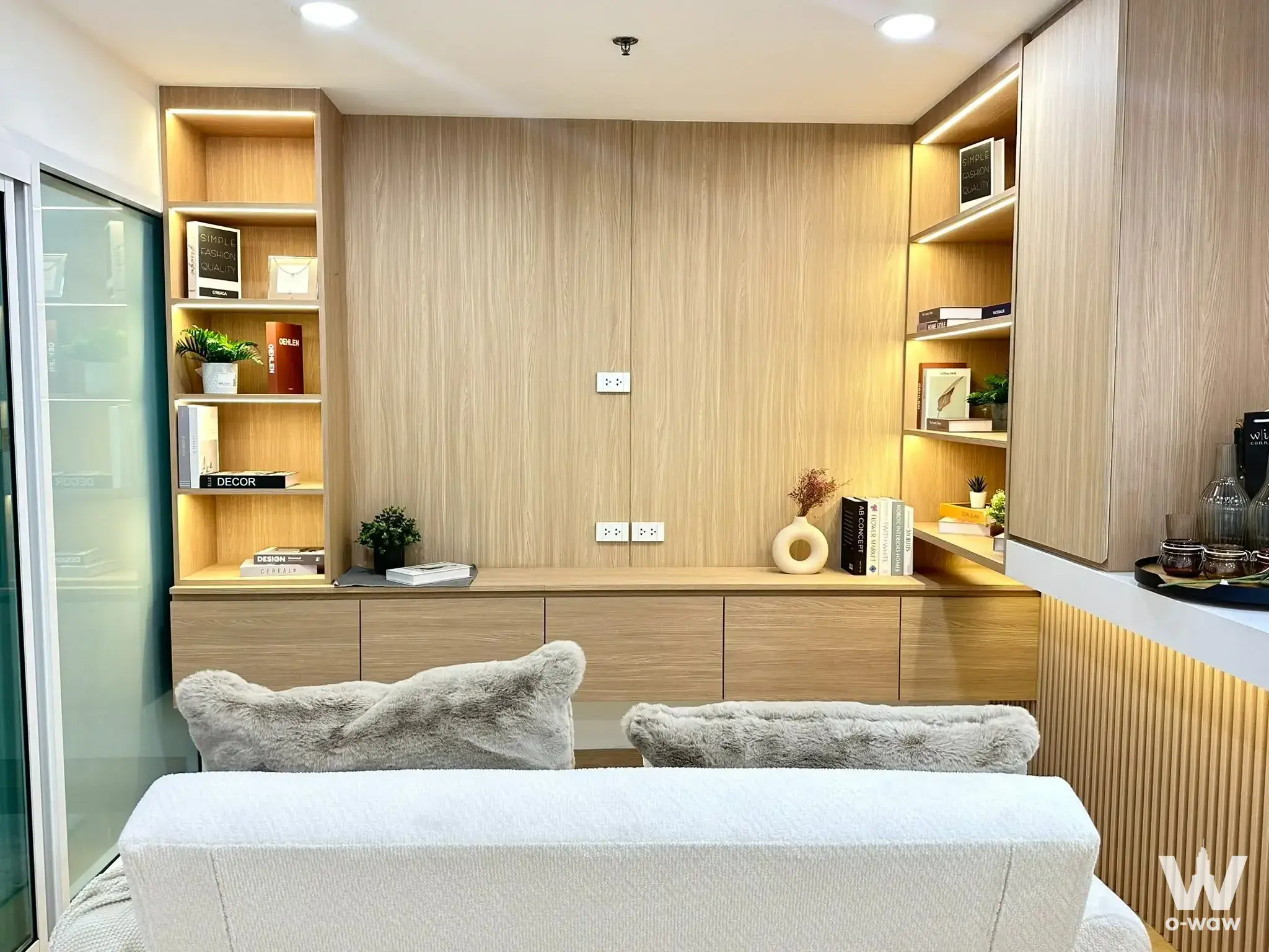 Modern living room with light oak cabinetry, LED shelving, and white sofa in Bangkok Horizon Ramkhamhaeng 1-bed condo for