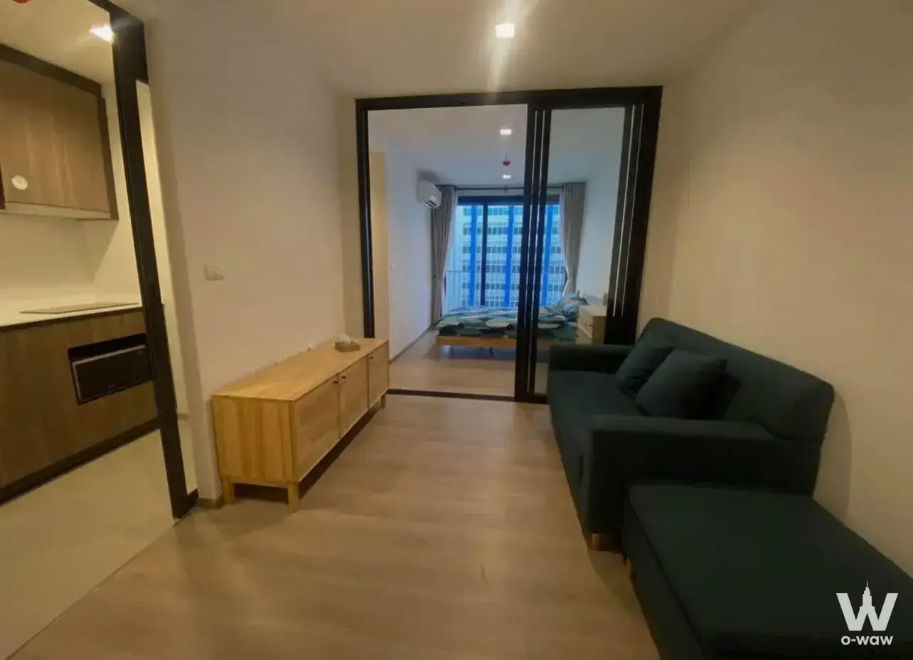 Open-plan living room in a THE LINE Phahonyothin Park condo featuring a teal sofa and glass partition