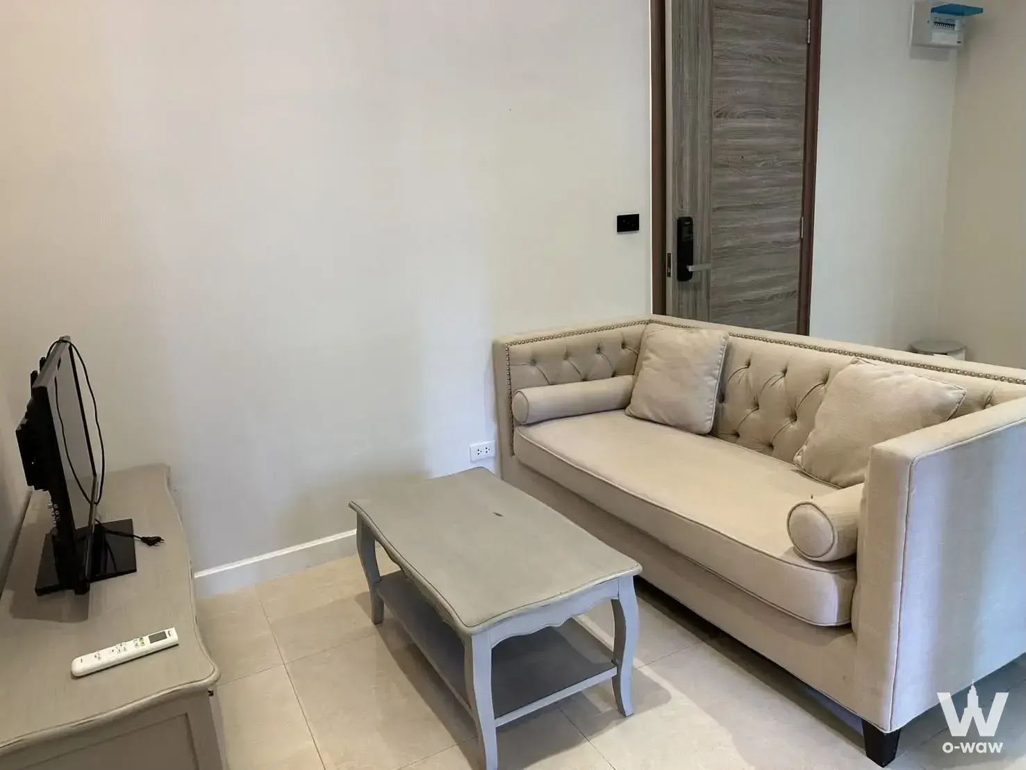 Modern living room in 1-bed Mayfair Place Sukhumvit 50 condo with cream sofa, grey coffee table, and smart lock door