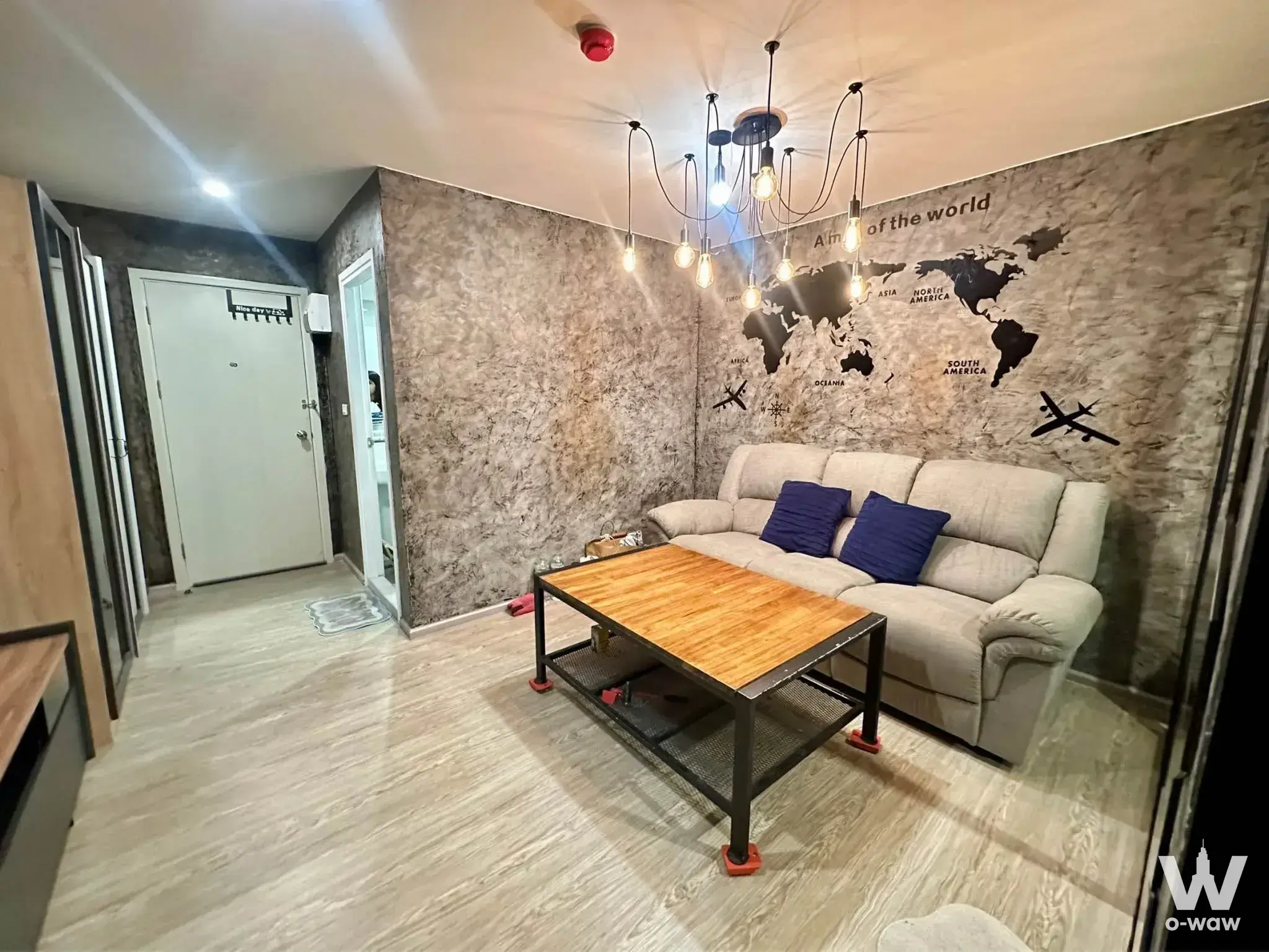 Stylish living room in รีช พหลโยธิน 52 condo with world map mural, industrial chandelier, and beige sofa