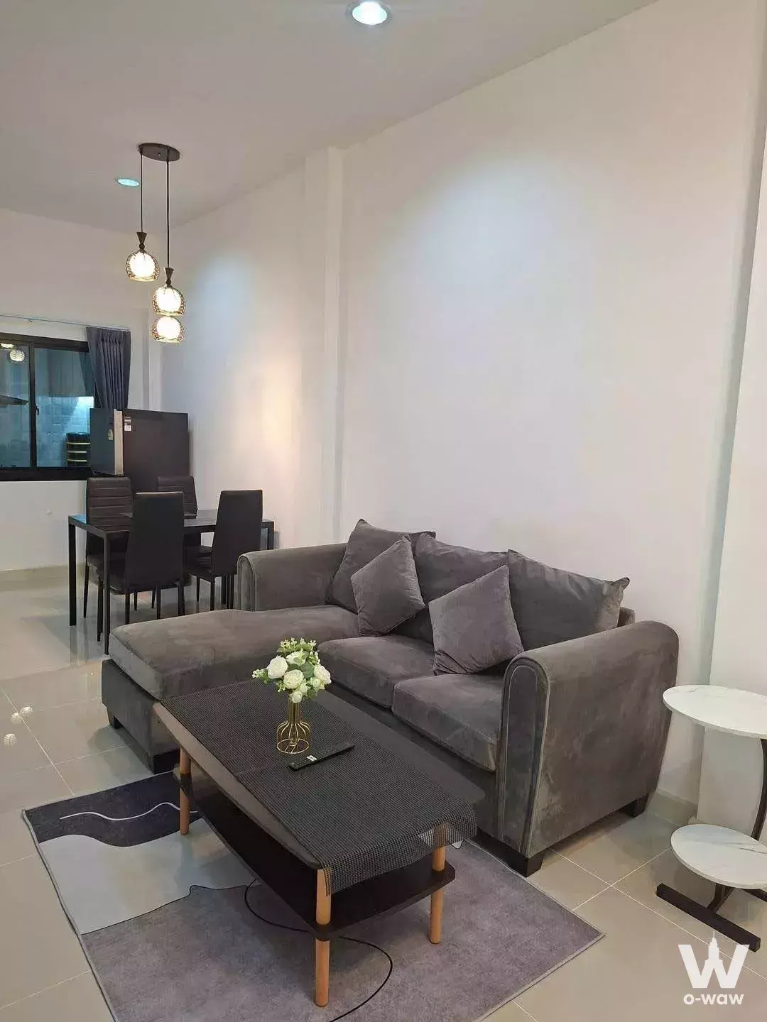 Modern living room in 2-bed condo for rent at Tiger Lane Sansiri with grey sectional sofa and glossy tile floors