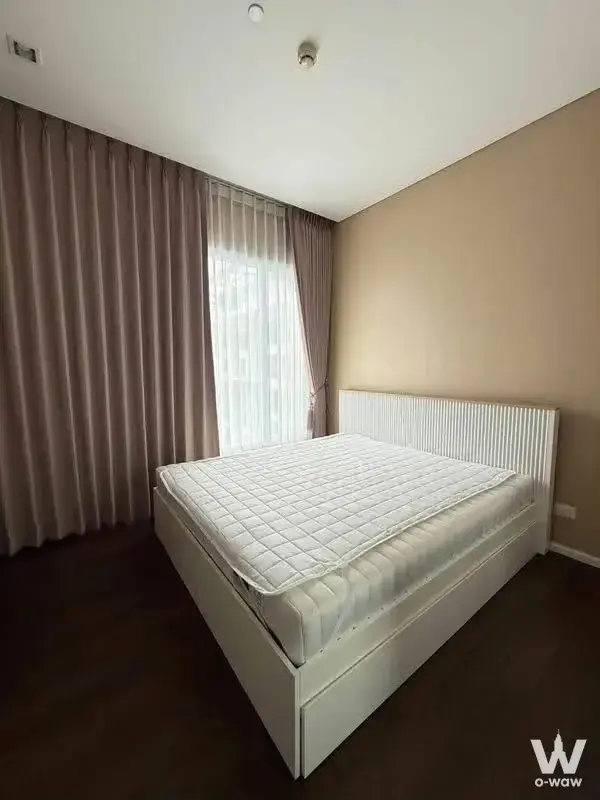 Minimalist bedroom in 2-bed Bangkok condo with wood floors, white fluted bed frame, and floor-to-ceiling drapes letting in