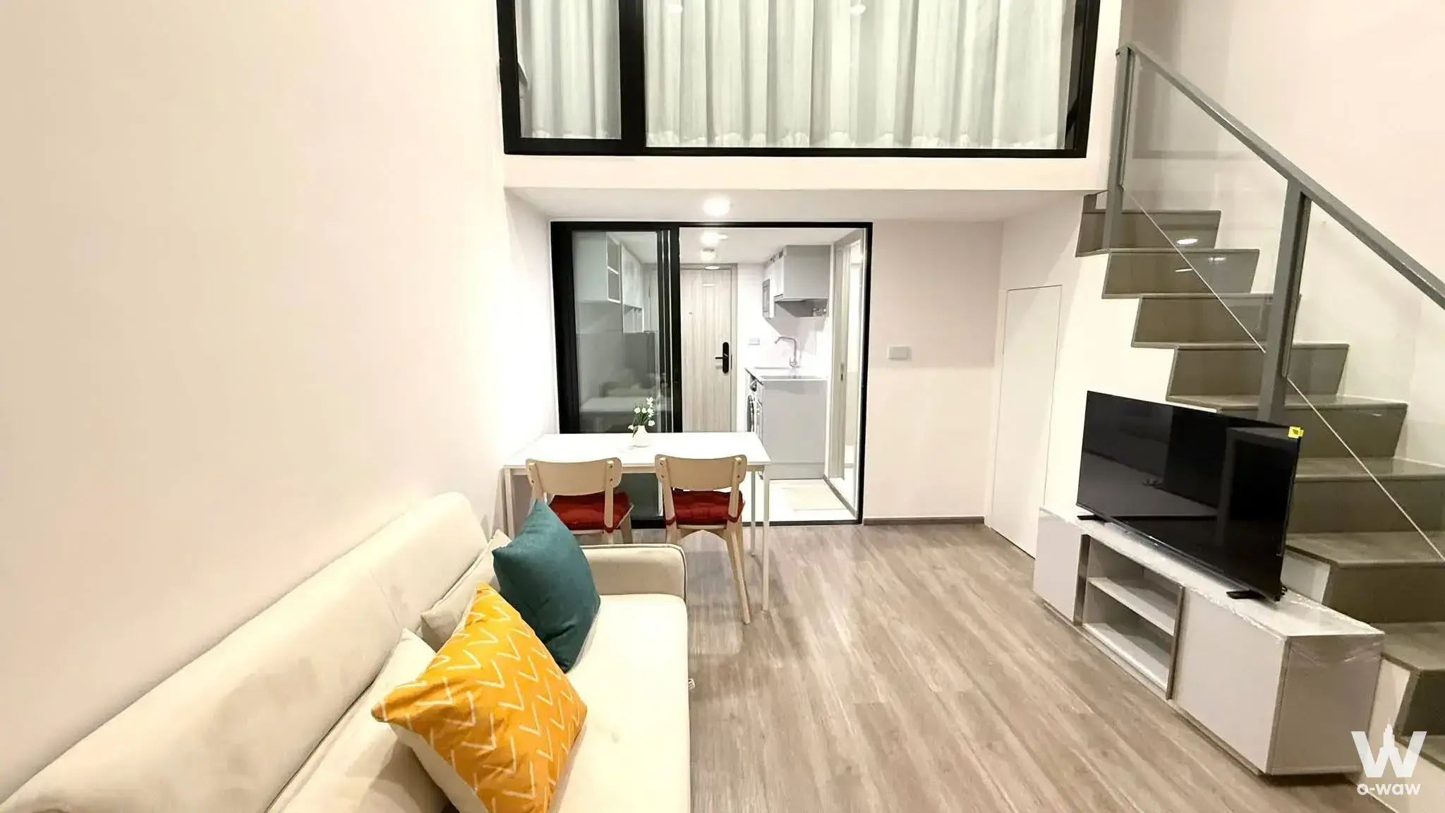 Modern living area in So Origin Kaset Interchange duplex with high ceilings, floating staircase, and open kitchen