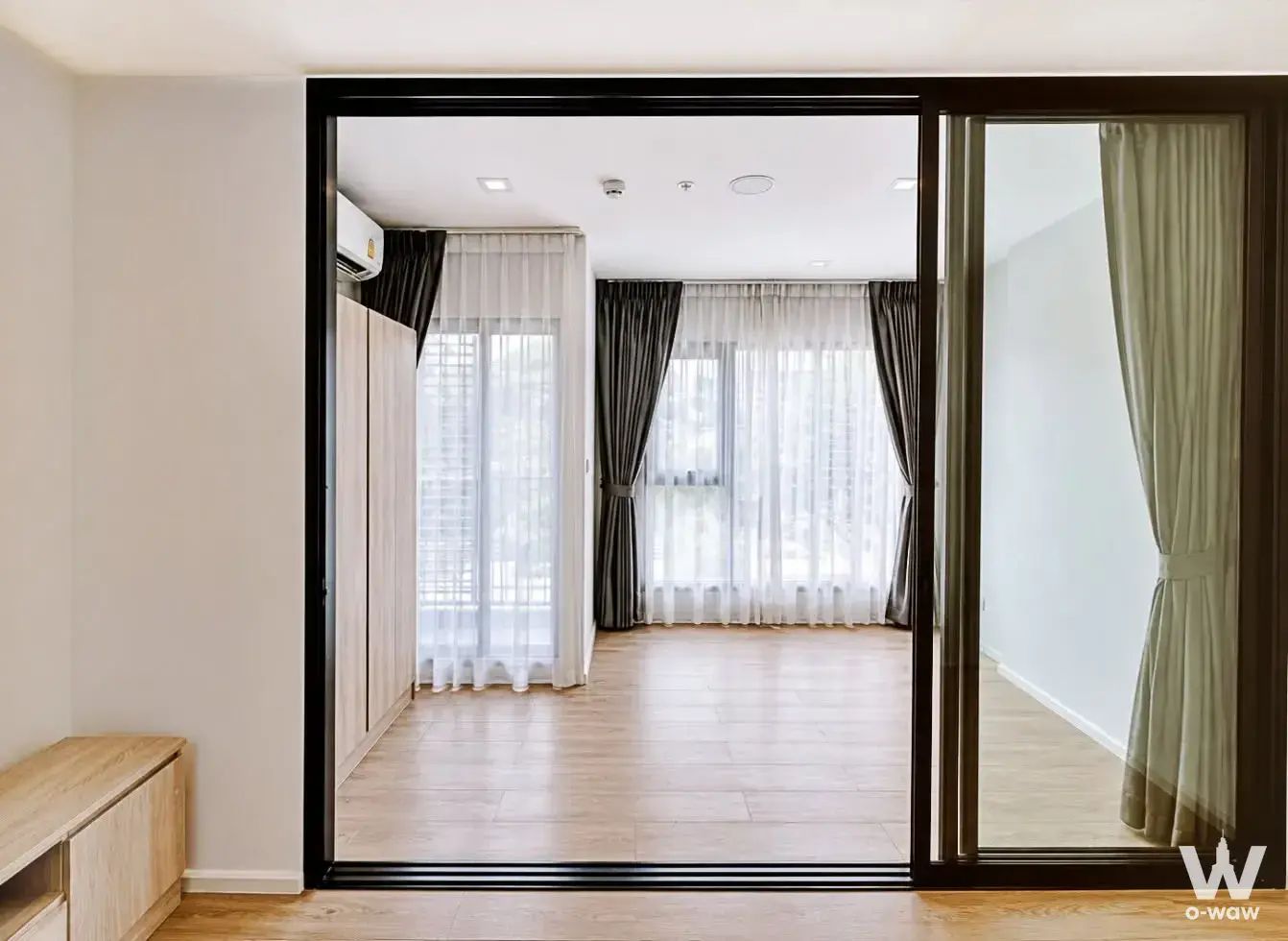 Unfurnished 1-bed condo living room in Modiz Sukhumvit 50 with light oak floors and black-framed glass doors
