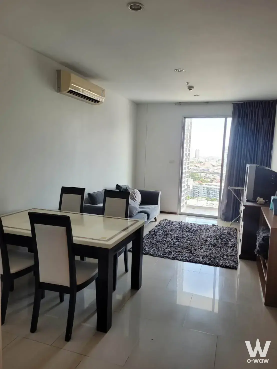 Villa Sathorn Condominium living area with grey sofa, dark wood dining table, and city skyline view