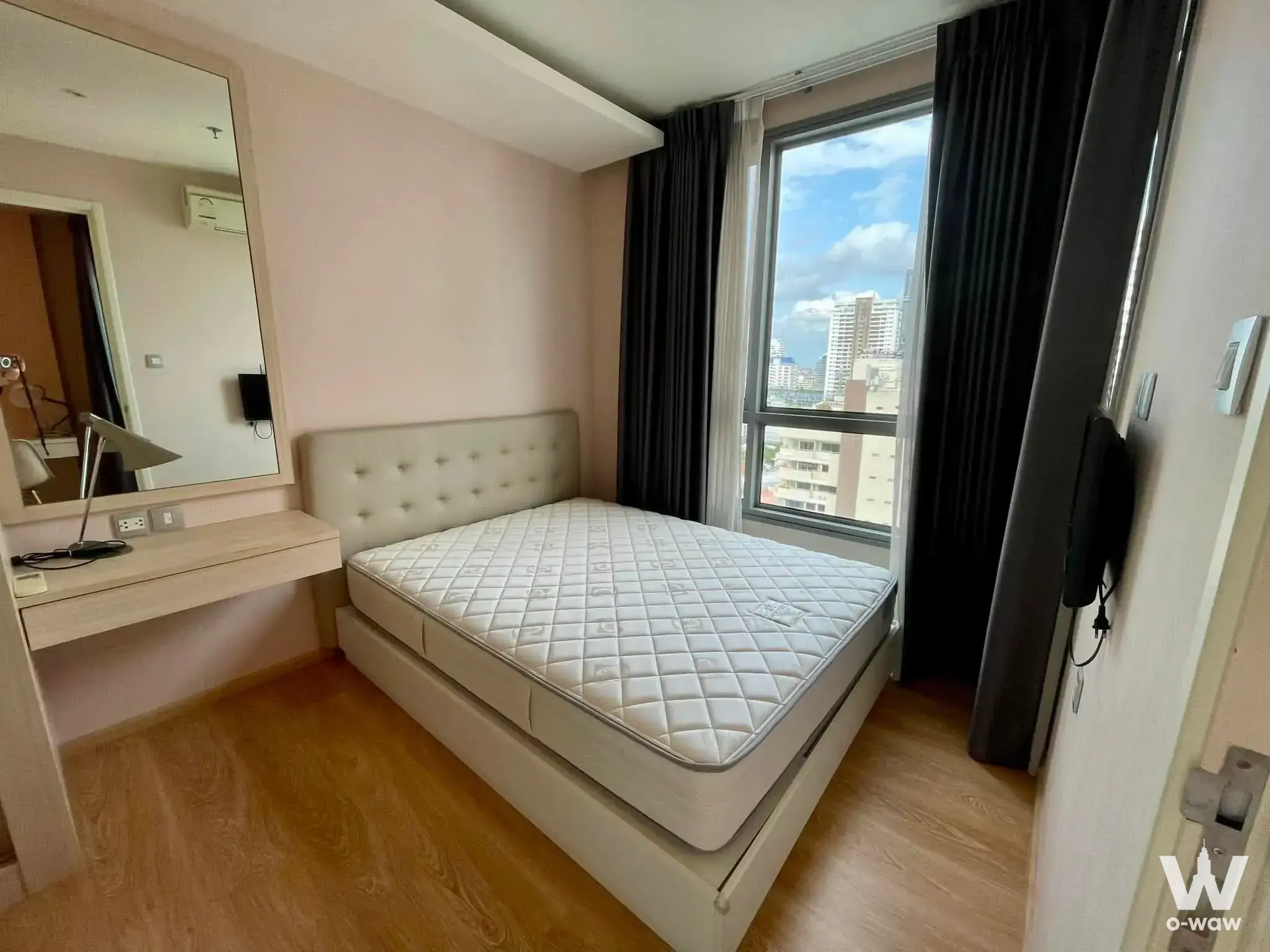Modern bedroom with pink walls, cream bed, floating desk, and city skyline view through large window