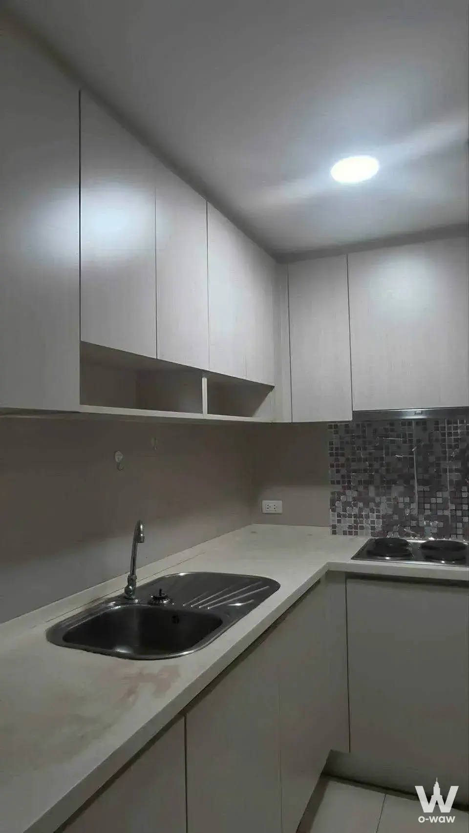 L-shaped kitchen with light-grey handleless cabinets, white countertop, mosaic backsplash, and built-in cooktop