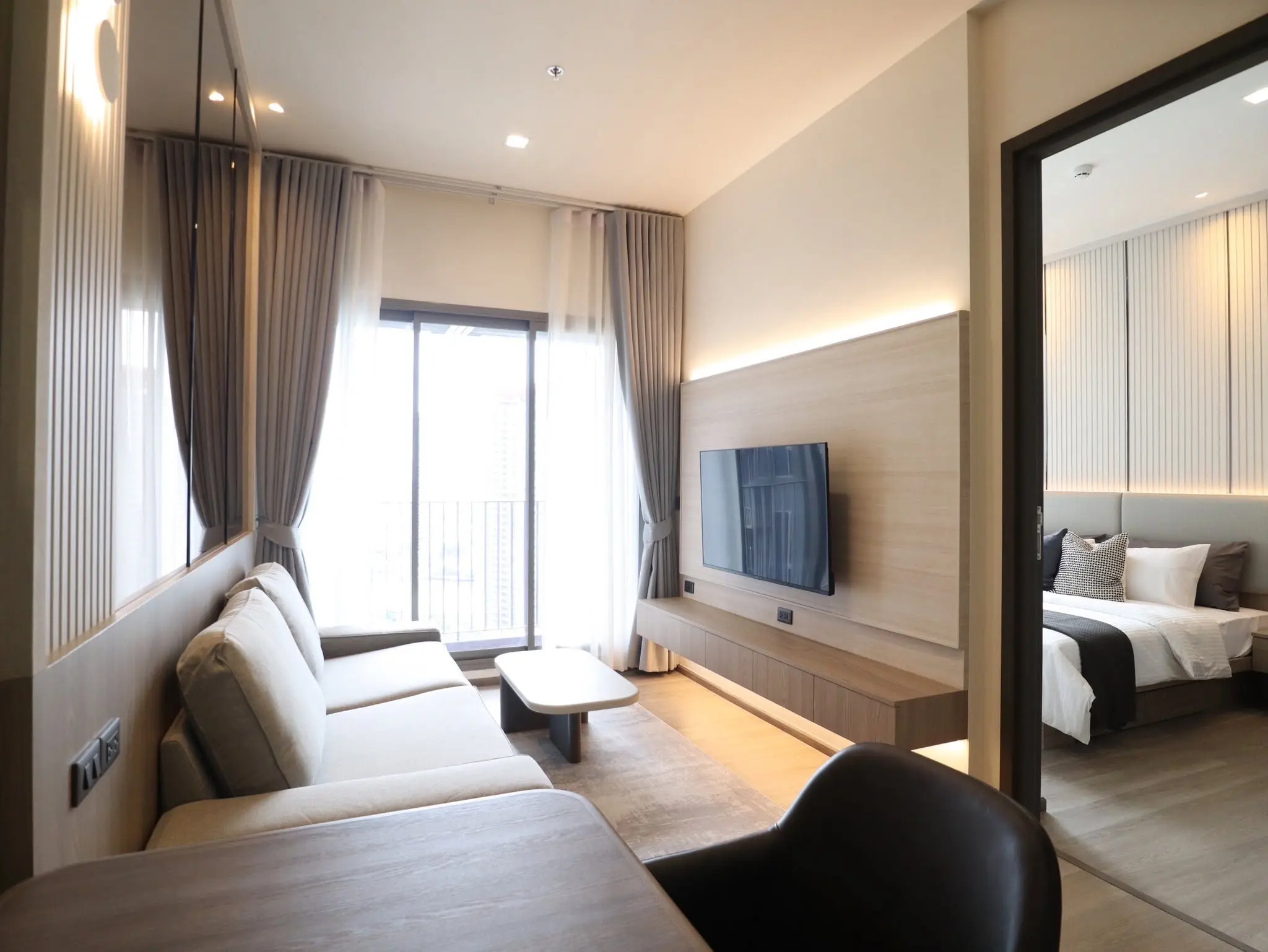 Modern living room in Rhythm Charoenkrung Pavillion condo featuring beige sofa and wood slat accent wall