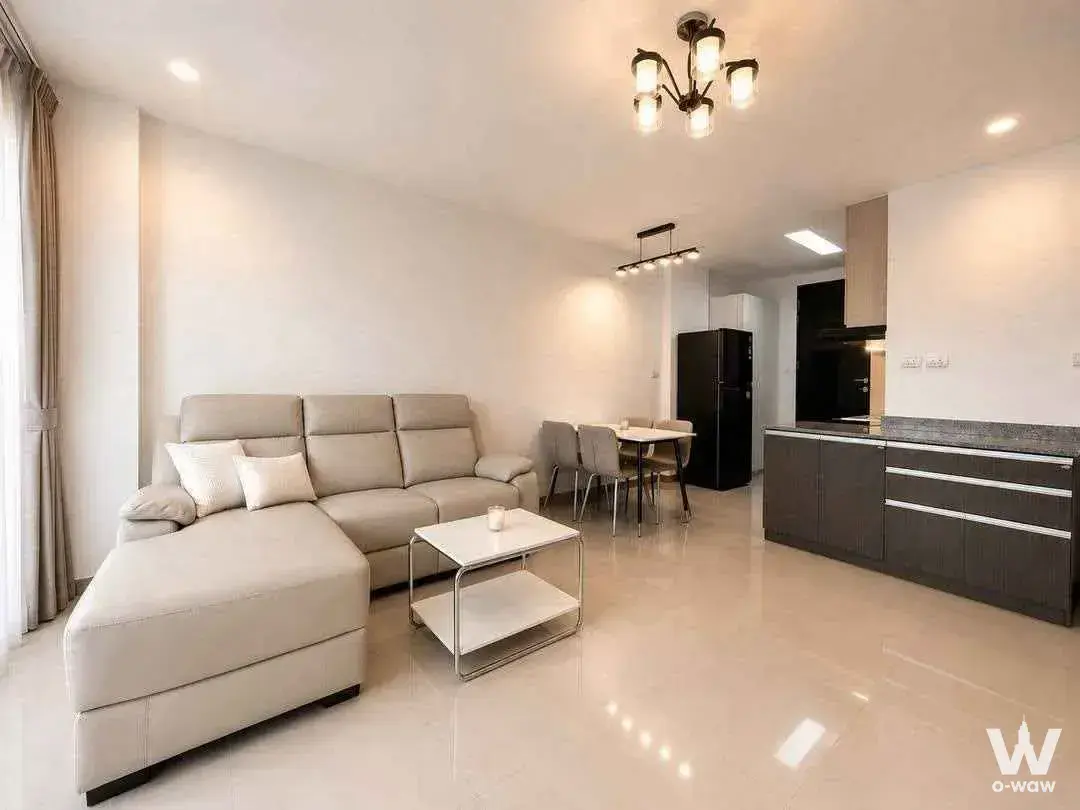 Modern open-plan living and dining area with beige sectional sofa, glossy tile floors, and dark grey kitchenette