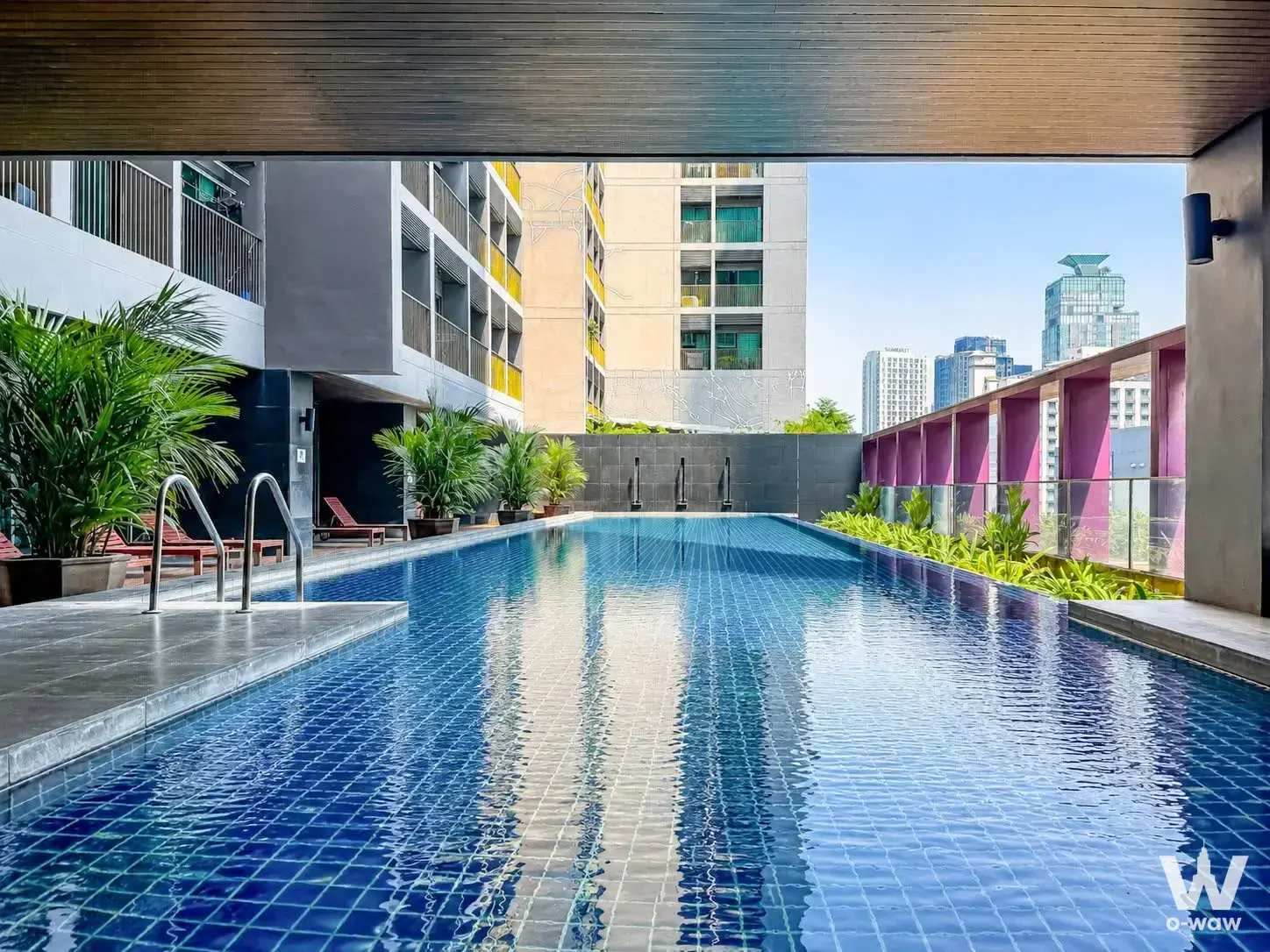 Rooftop pool deck in Noble Remix with wooden loungers and Bangkok skyline view