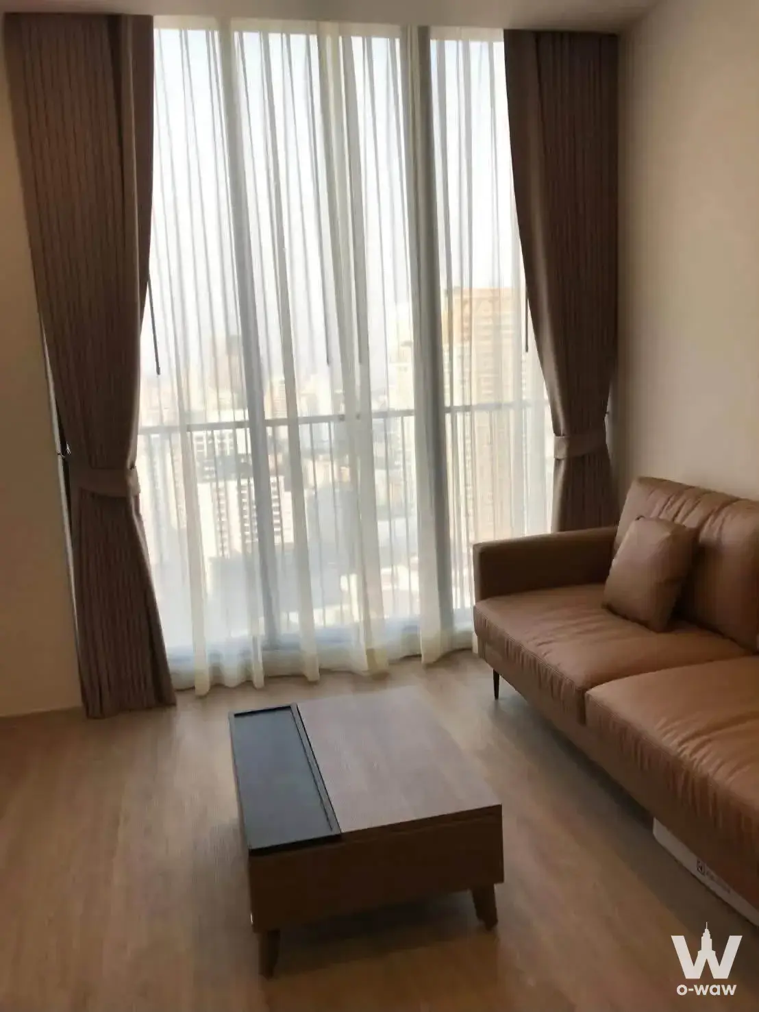 Bright living room in a 2-bed Noble State 39 condo featuring tan leather sofa and floor-to-ceiling windows with city views