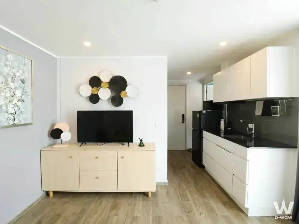 Open-plan living room with light wood floors and modern kitchen in NOON Village Tower 2 condo for rent