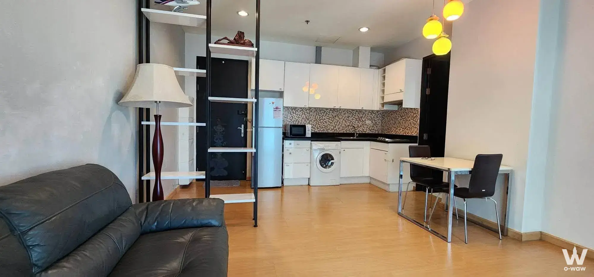 Modern 1-bed condo living room in Siam-Pathum Wan with grey sofa, wood floors and open kitchen