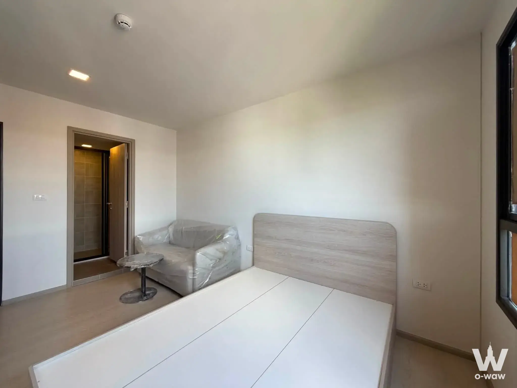 Bright 1-bed condo bedroom in dcondo air Ladkrabang with pale wood floors, grey headboard bed, and marble side table