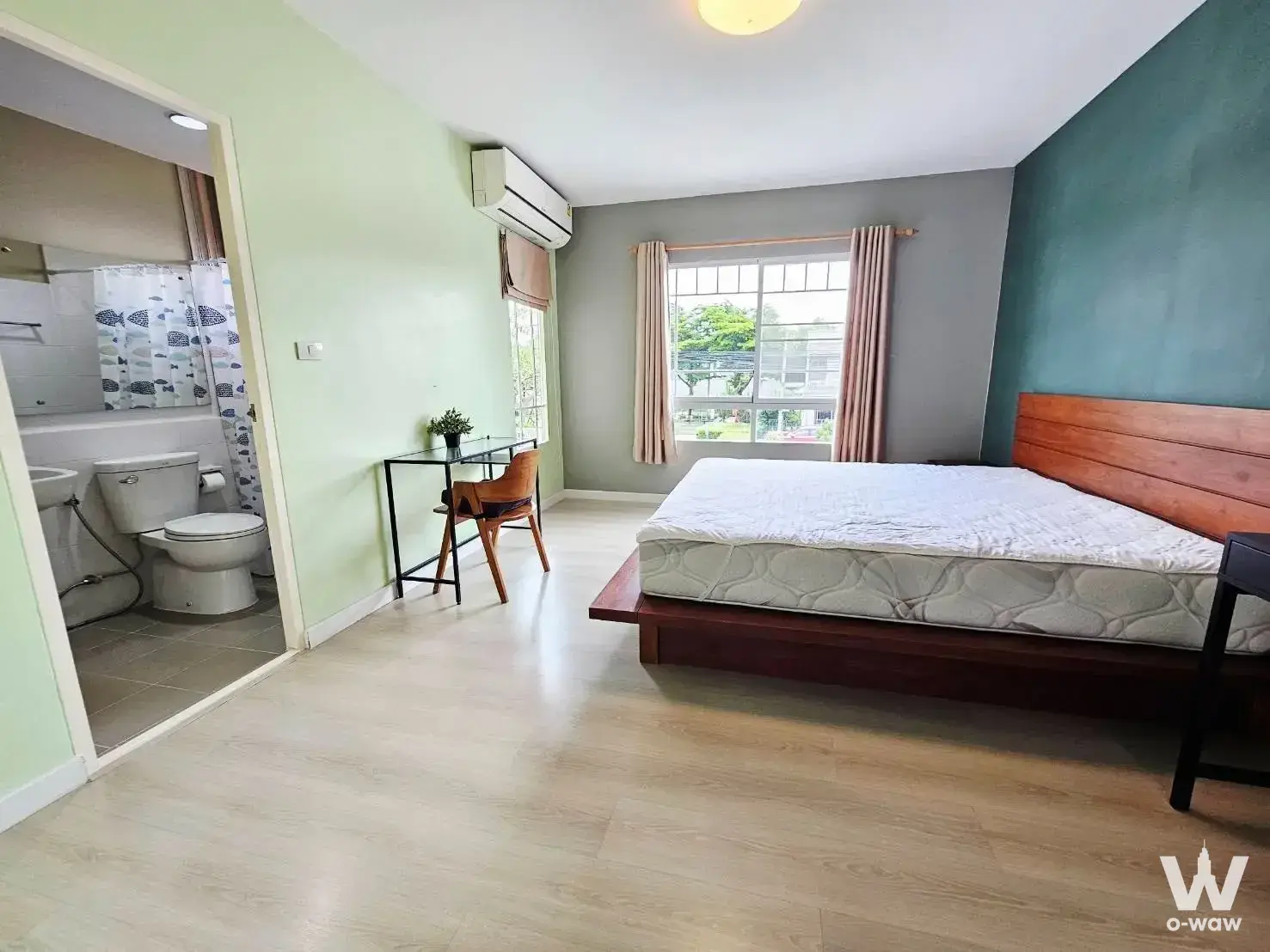 Modern bedroom in 2-bed Indy 2 Bangna townhouse with teal accent wall, wooden bed, and attached bathroom
