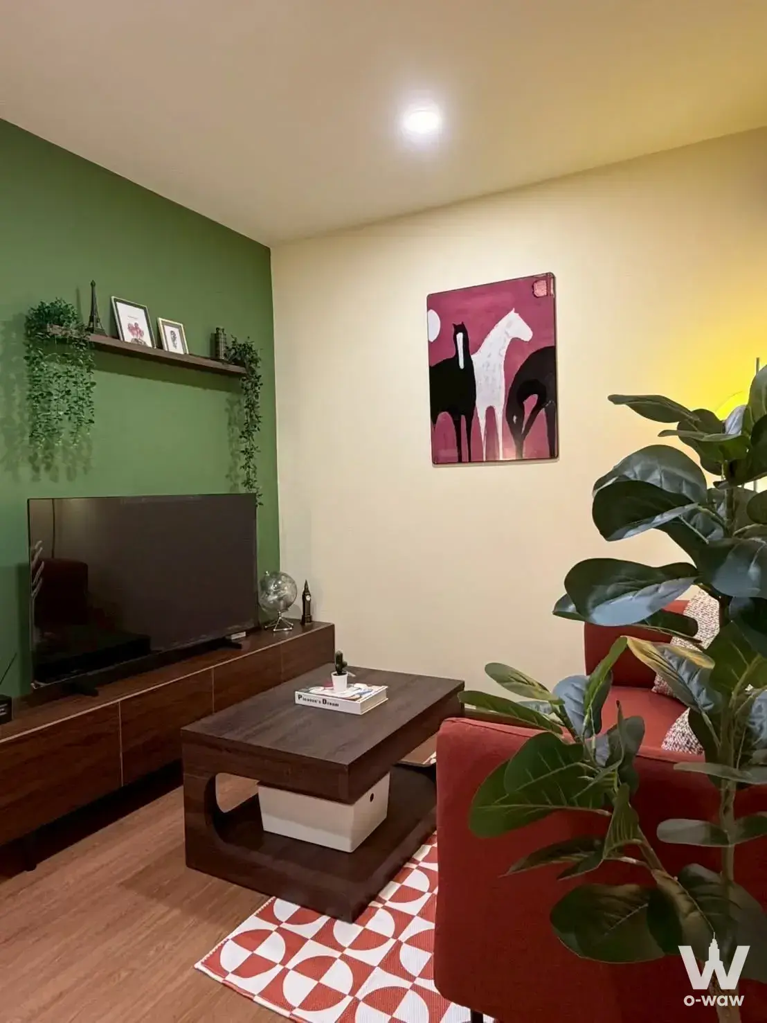 Modern living room in 1-bed condo for sale at The Parkland Srinakarin Lakeside with green accent wall and fiddle-leaf fig