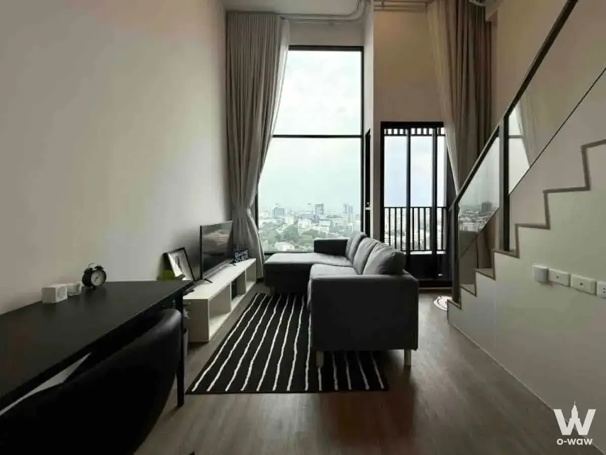 Modern duplex living room with city views, grey sofa, and glass staircase in So Origin Kaset Interchange