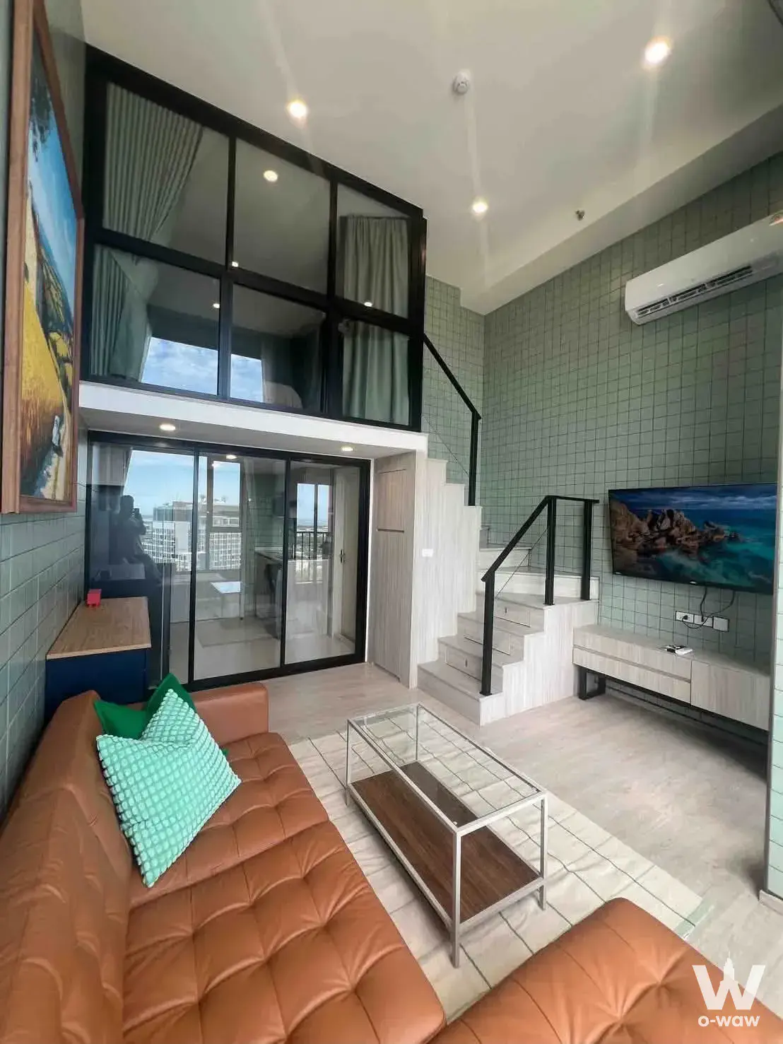 Modern loft living room with sage green tiles, leather sofa, and mezzanine in 1-bed condo for rent at Origin Plug & Play E22
