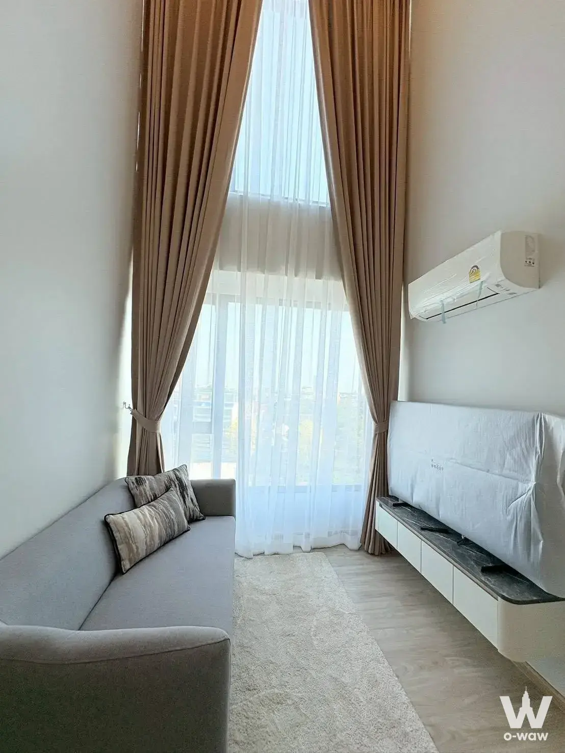 Bright living room in a 2-bed ESQUE Condo Sukhumvit 101/1 rental with floor-to-ceiling windows and a light-grey sofa