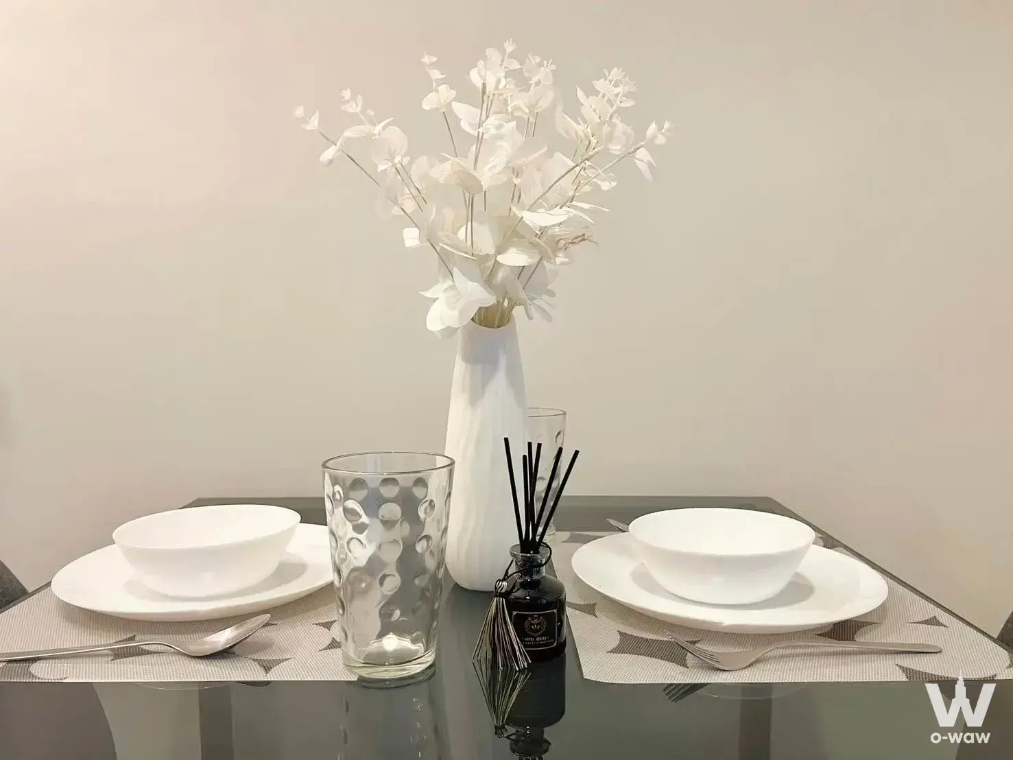 Glossy black glass dining table set for two with white eucalyptus centerpiece in modern 1-bed condo for rent in Chewathai