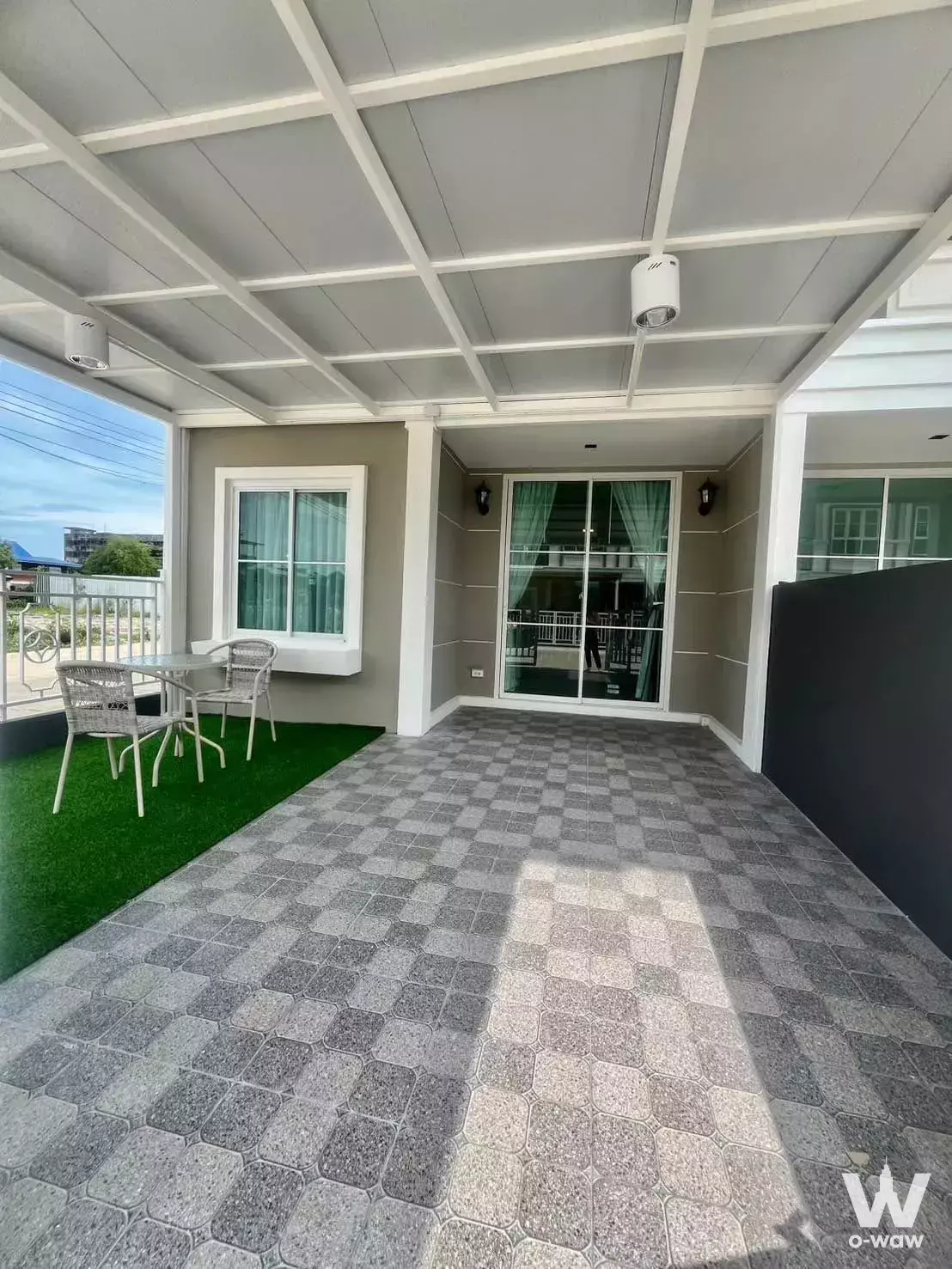 Spacious covered terrace with grey pavers, green turf, and white wicker dining set in 2-bed house for rent at ICOPENH