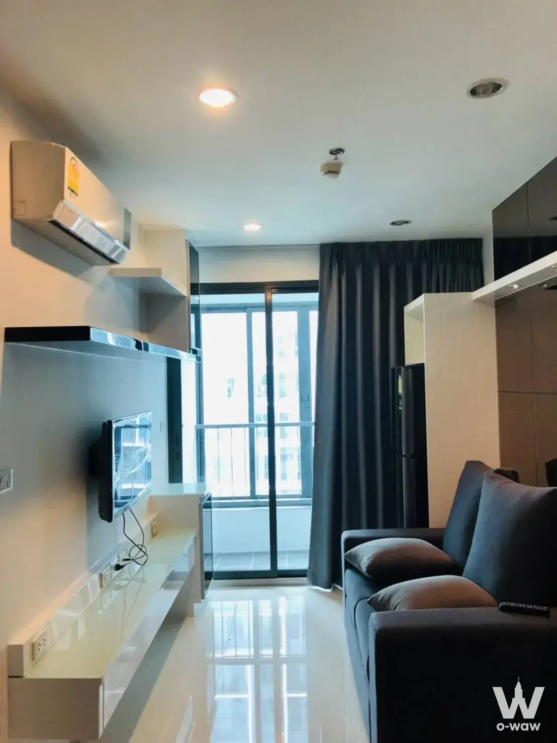 Living room in an Ideo Mobi Charan Interchange condo with a grey sofa and floor-to-ceiling balcony doors