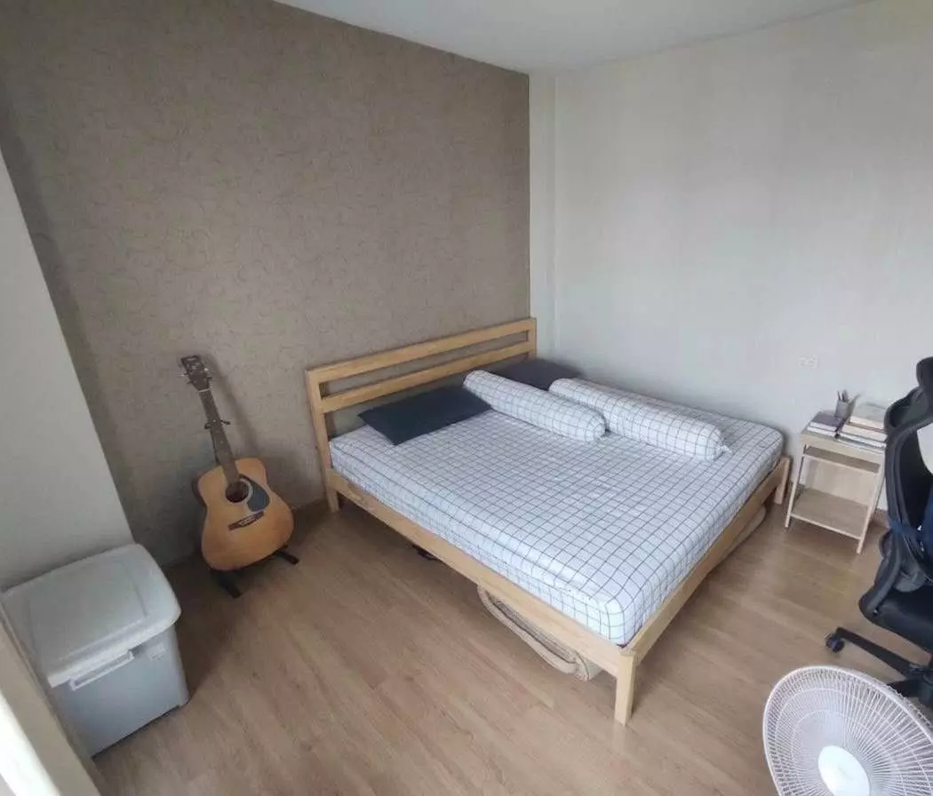Sparsely furnished bedroom with light wood flooring and textured beige accent wall in 2-bed condo for rent Supalai Park