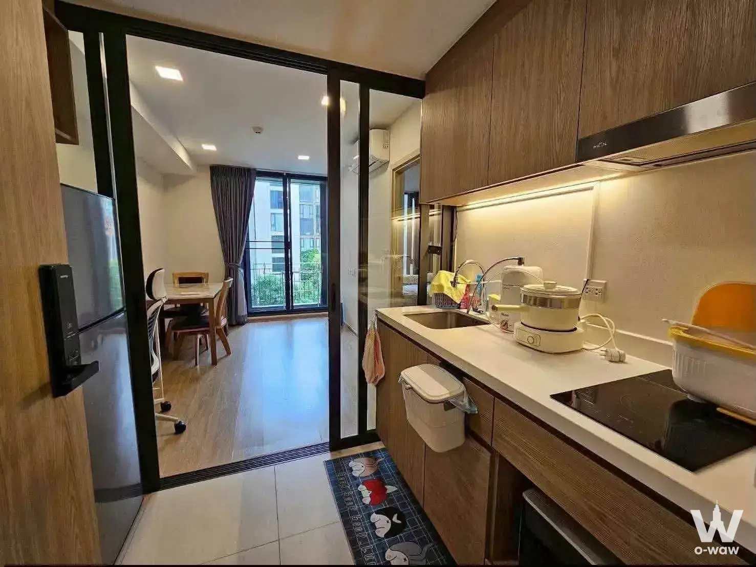Modern open-plan kitchen and dining area with light wood flooring, wooden cabinetry, and sliding glass doors leading to a