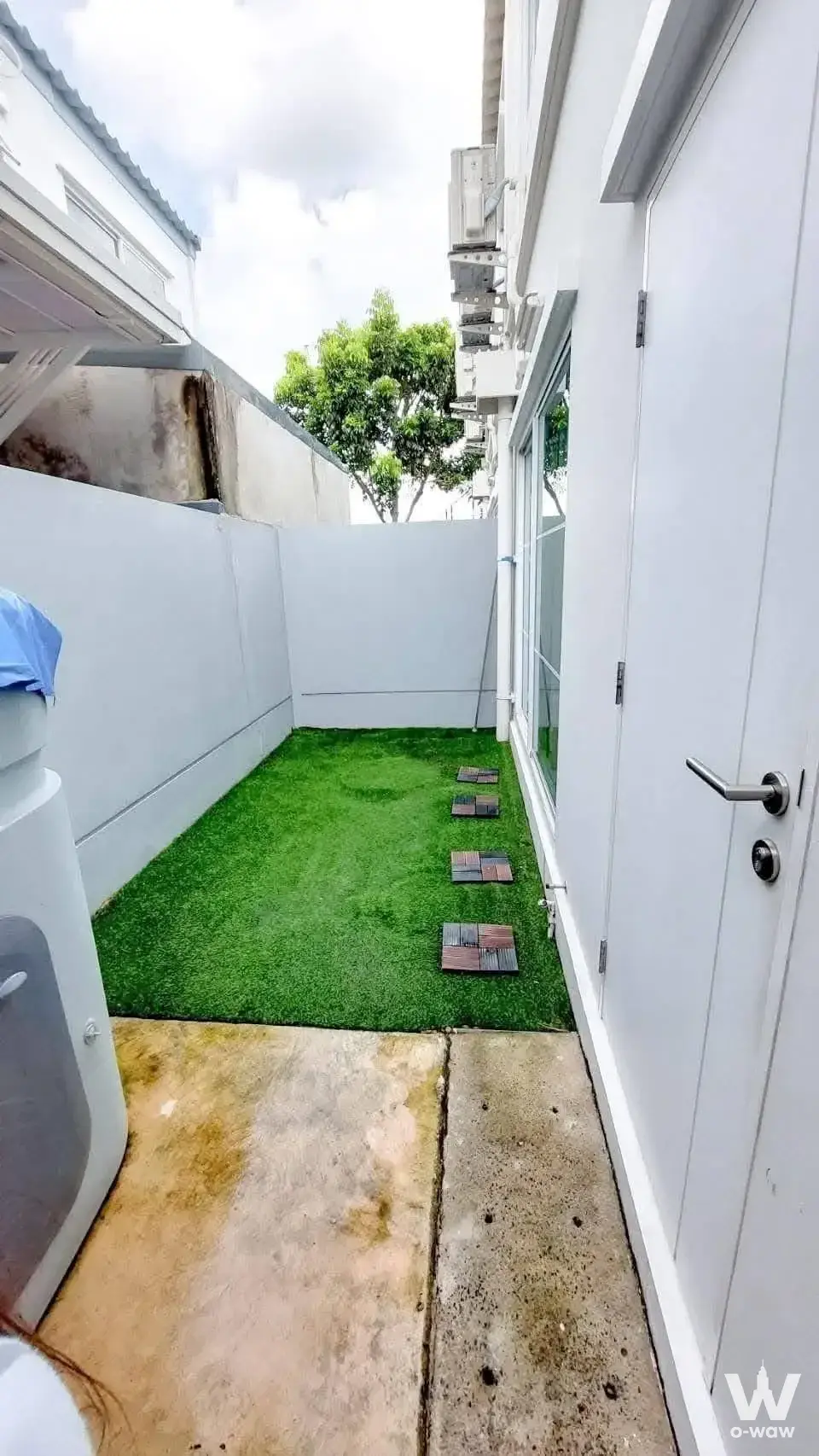 Private side yard of a Villaggio 2 Srinakarin-Bangna house featuring artificial turf, stepping stones, and white privacy